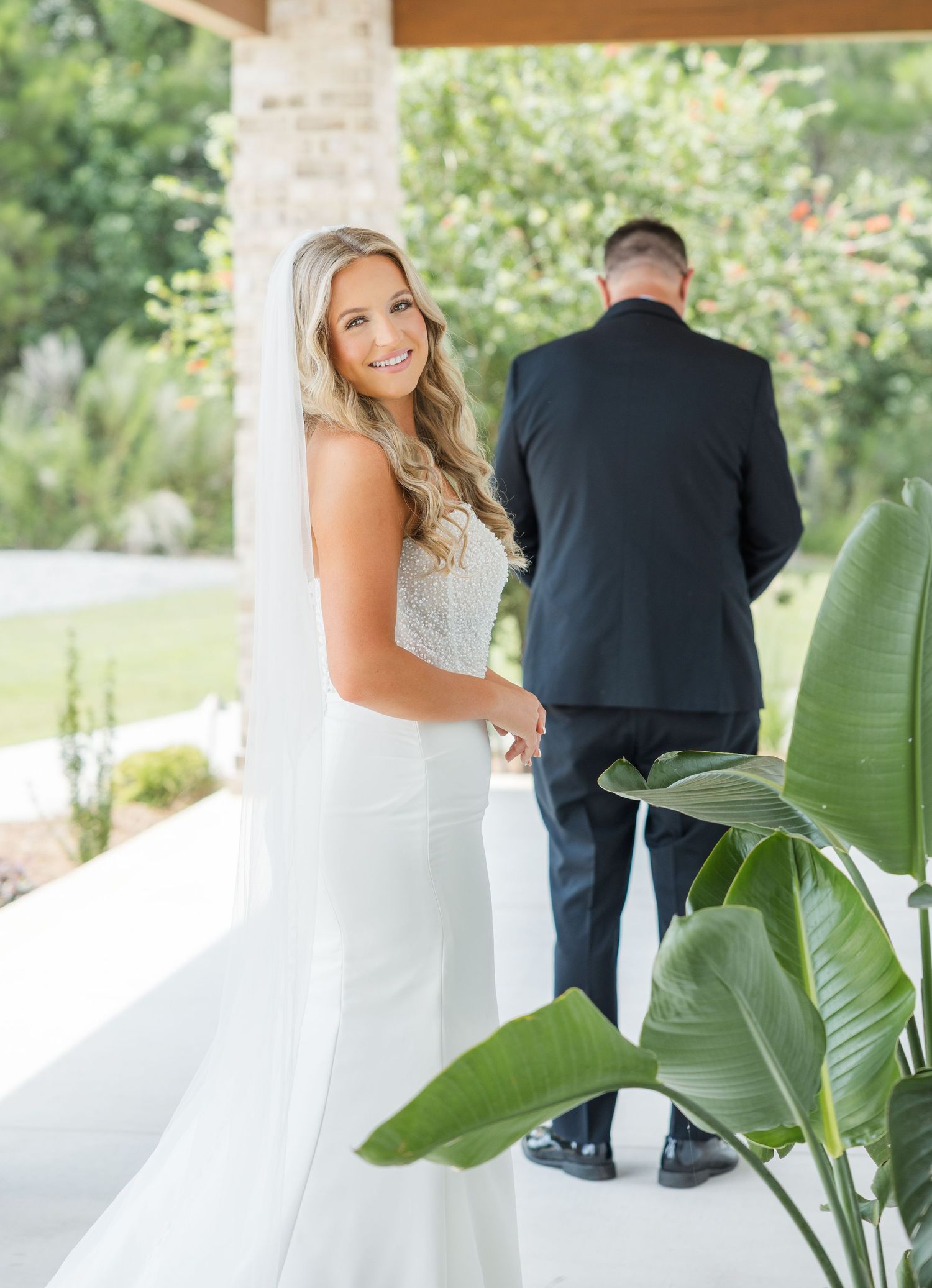 Bride in white gown and veil smiling during first look moment with groom on venue porch.