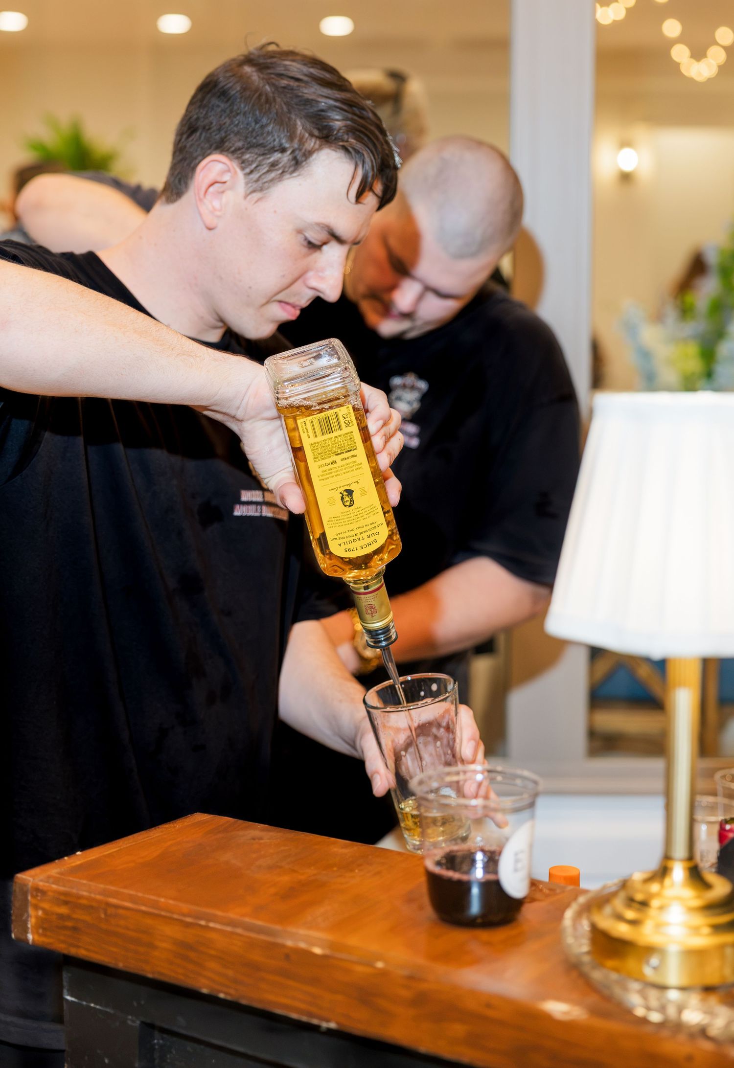 Bartender pouring whiskey from a bottle into a glass at a stylish bar event with warm lighting.