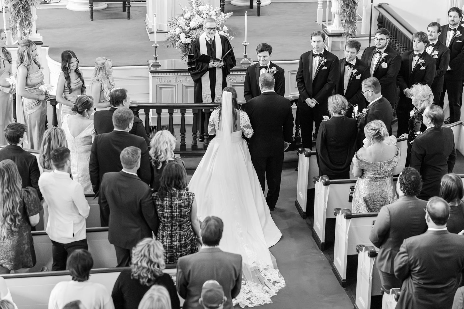 Black and white photo of a bride walking down the aisle at a church wedding ceremony with guests standing.