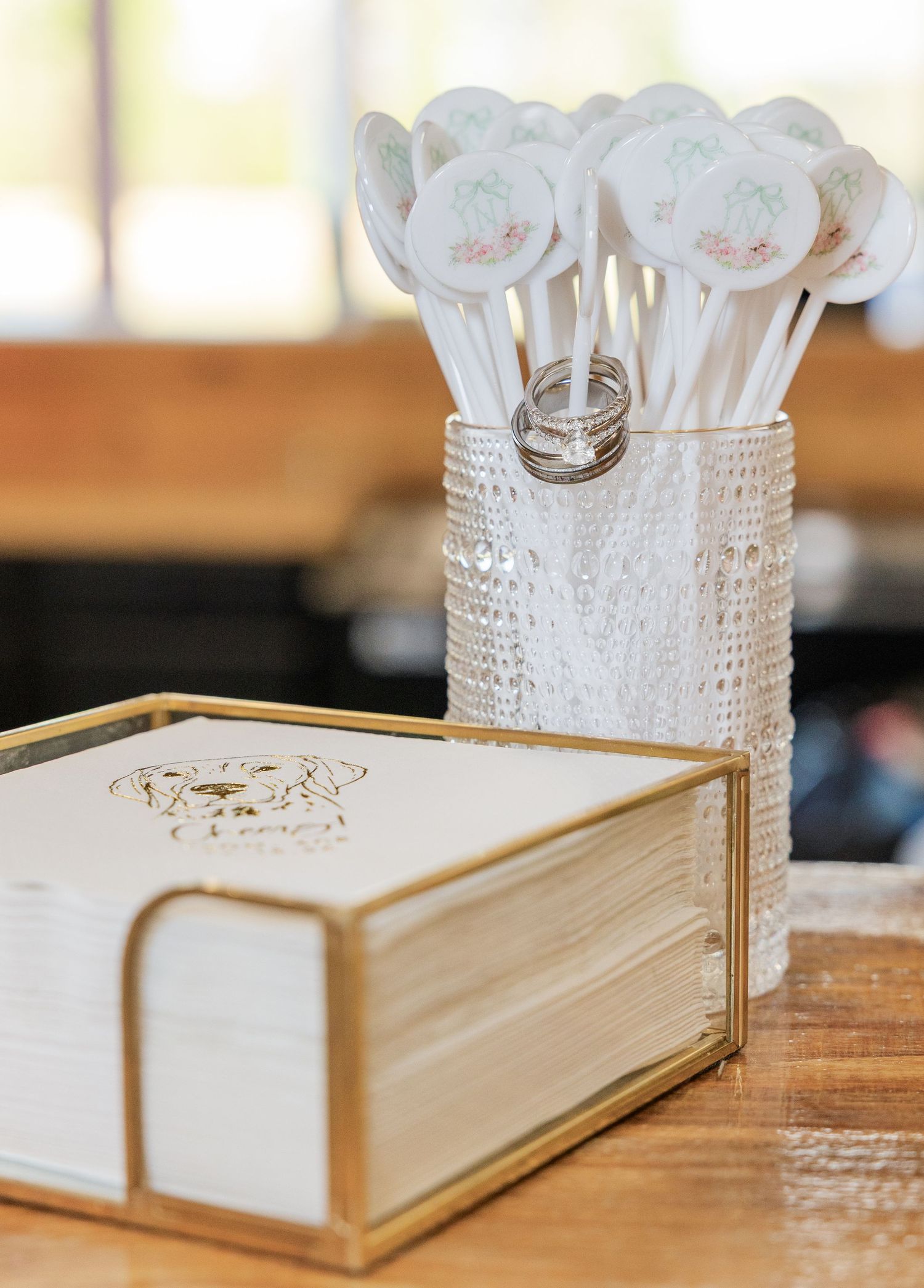 Wedding reception table with custom drink stirrers in glass vase and gold napkin holder.