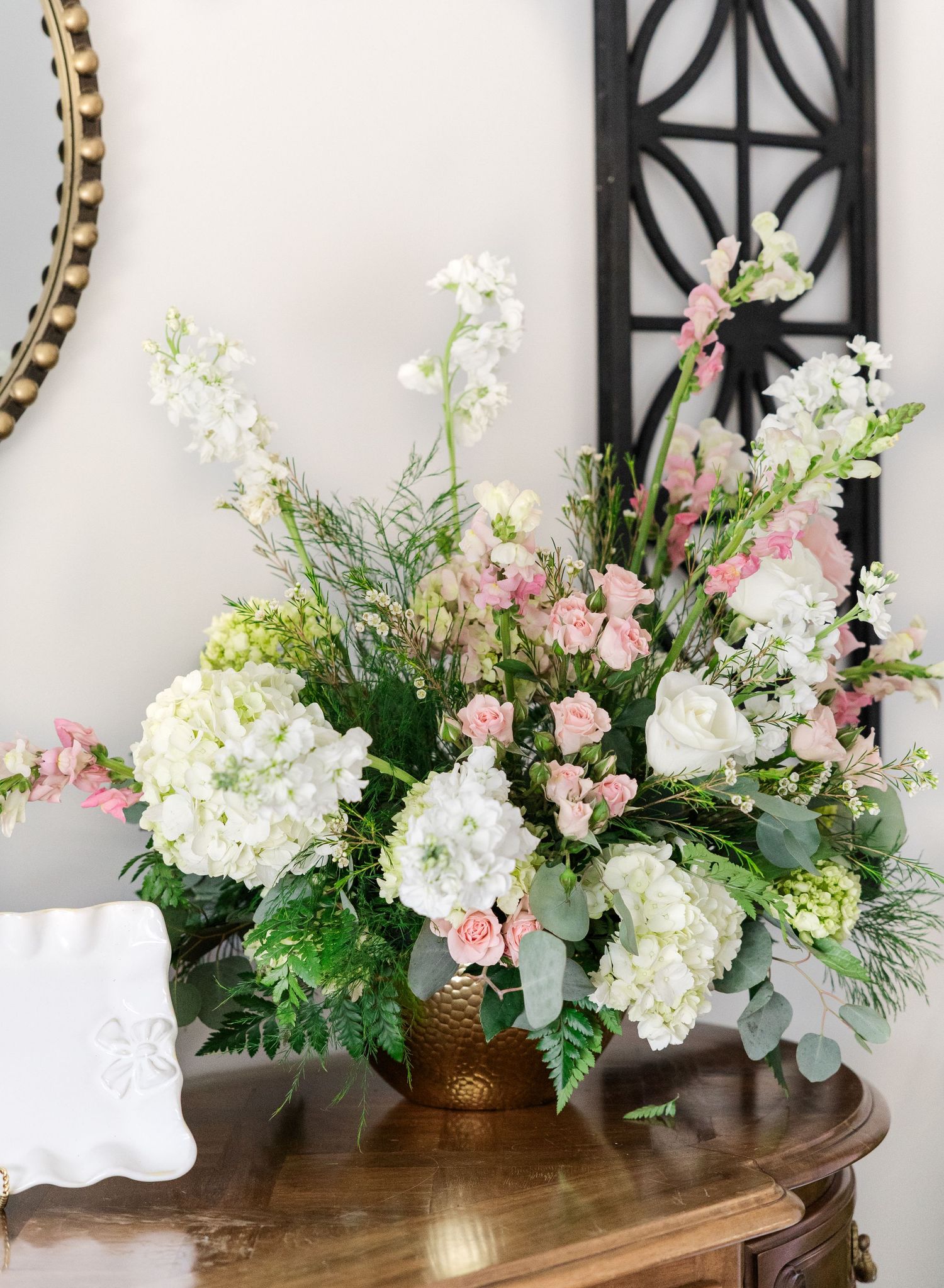 Elegant floral arrangement with white hydrangeas and pink blooms in a gold vase on a wooden table.