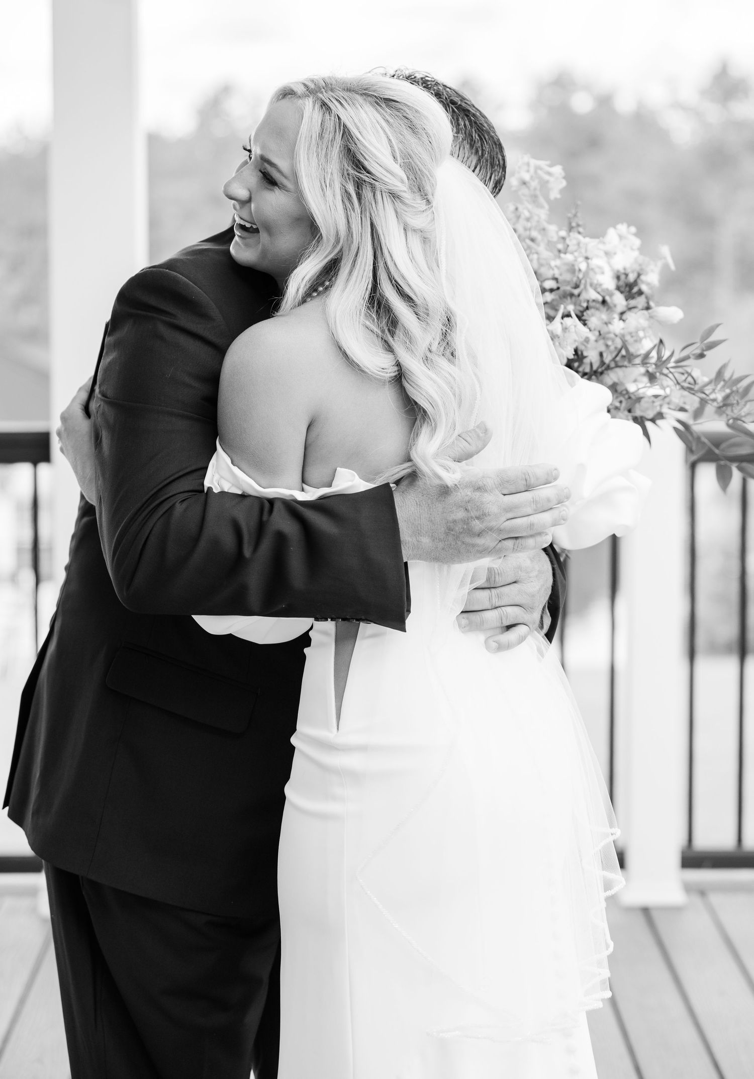 Black and white photo of bride and father sharing a heartfelt hug during wedding first look on deck.
