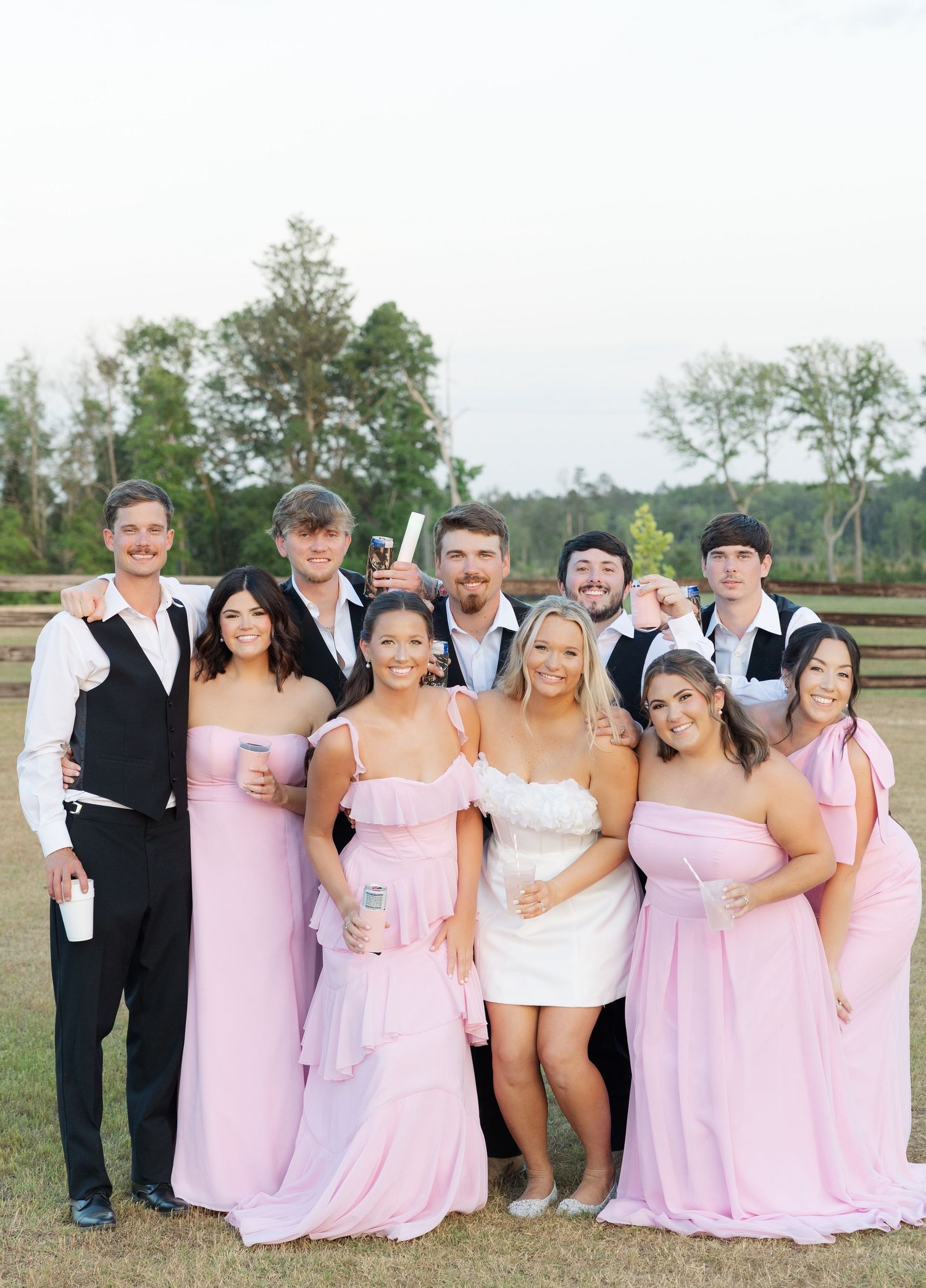 Wedding party group photo with bridesmaids in pink gowns and groomsmen in black attire.