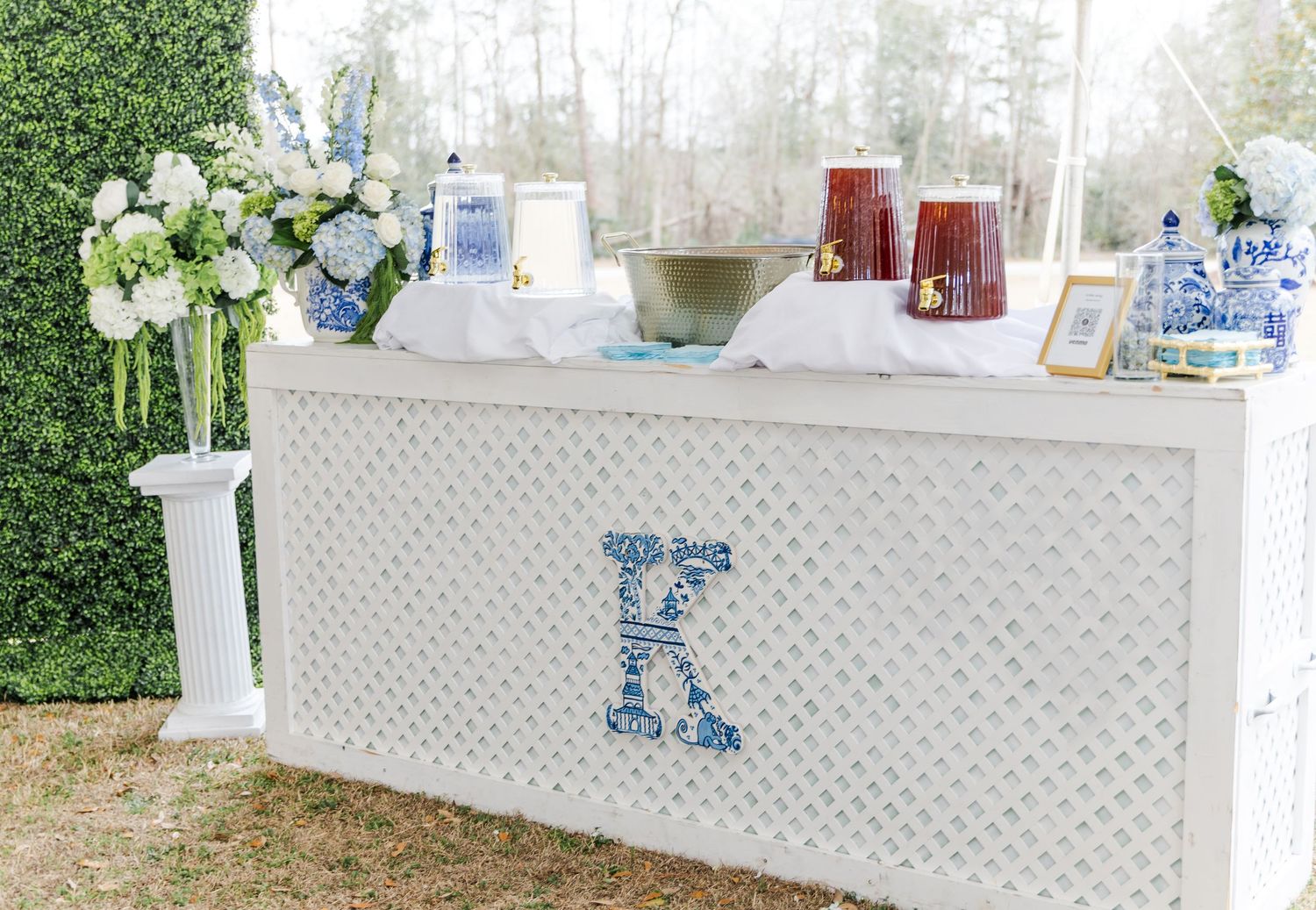 White lattice bar with blue monogram K letter, adorned with hydrangeas, candles, and blue and white ginger jars.