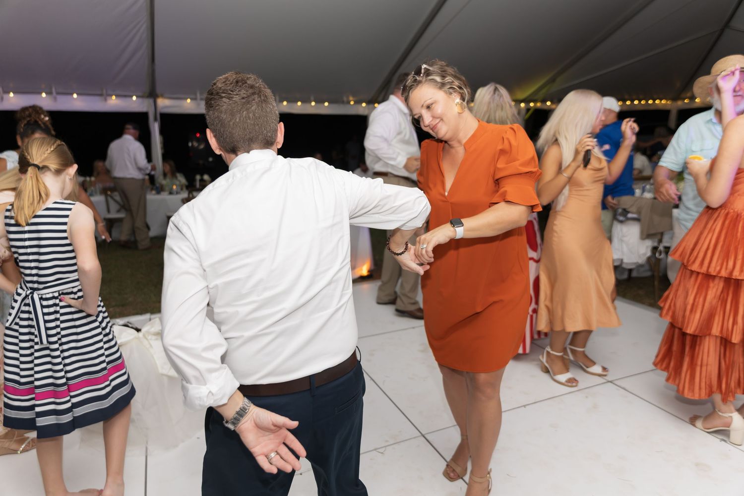 Wedding guests dancing and socializing on a dance floor under string lights.