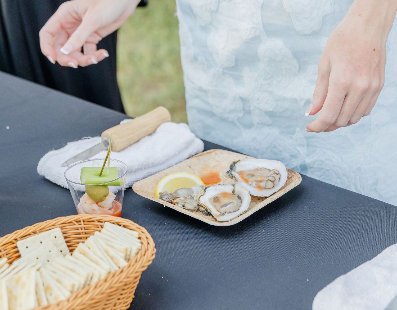Fresh oysters on ice are served with lemon wedges and condiments in a woven basket at an outdoor restaurant setting.