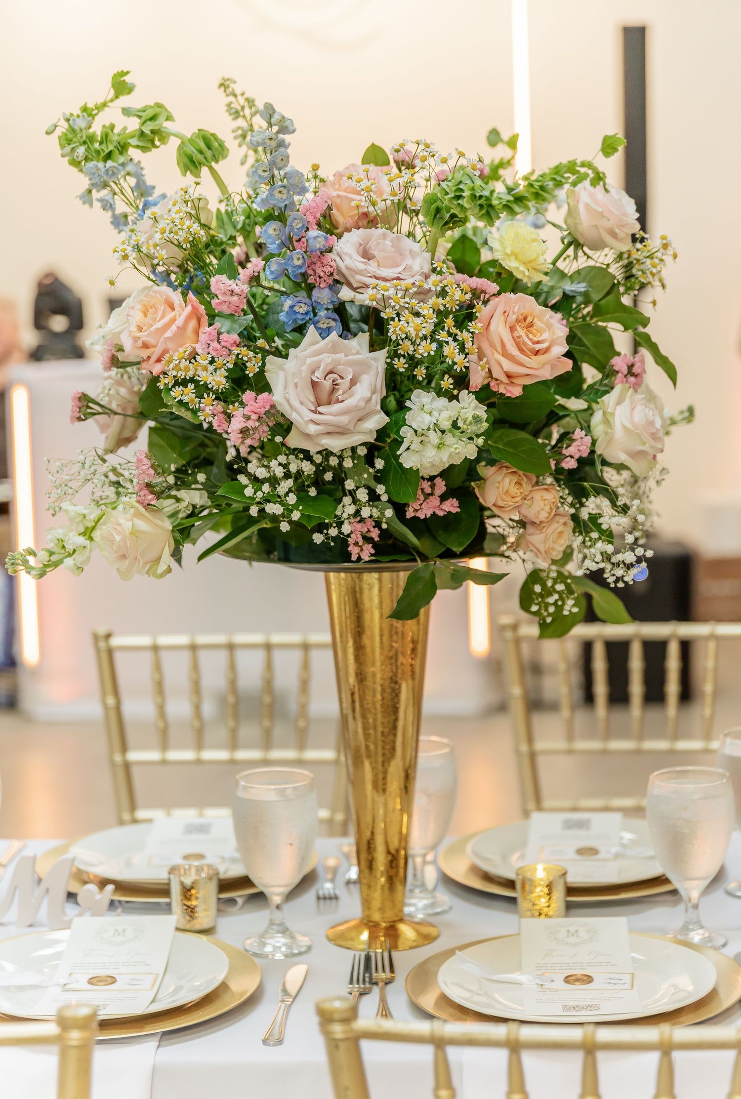 Wedding table setting with gold vases filled with pink roses, white hydrangeas and delicate greenery arrangements.