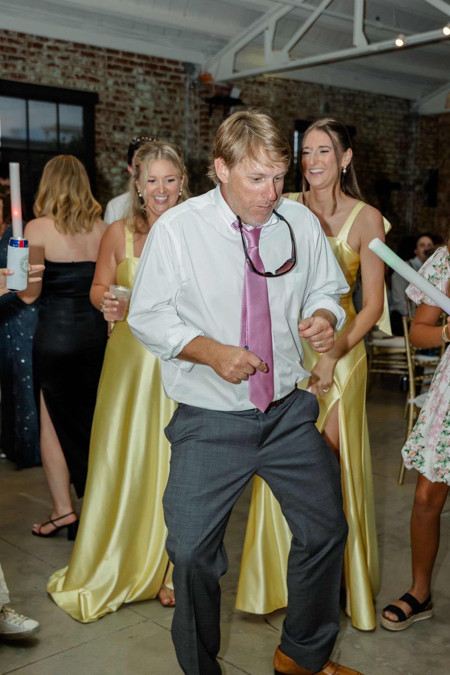 Guests dance and enjoy themselves on the reception dance floor with yellow decor visible in the background.