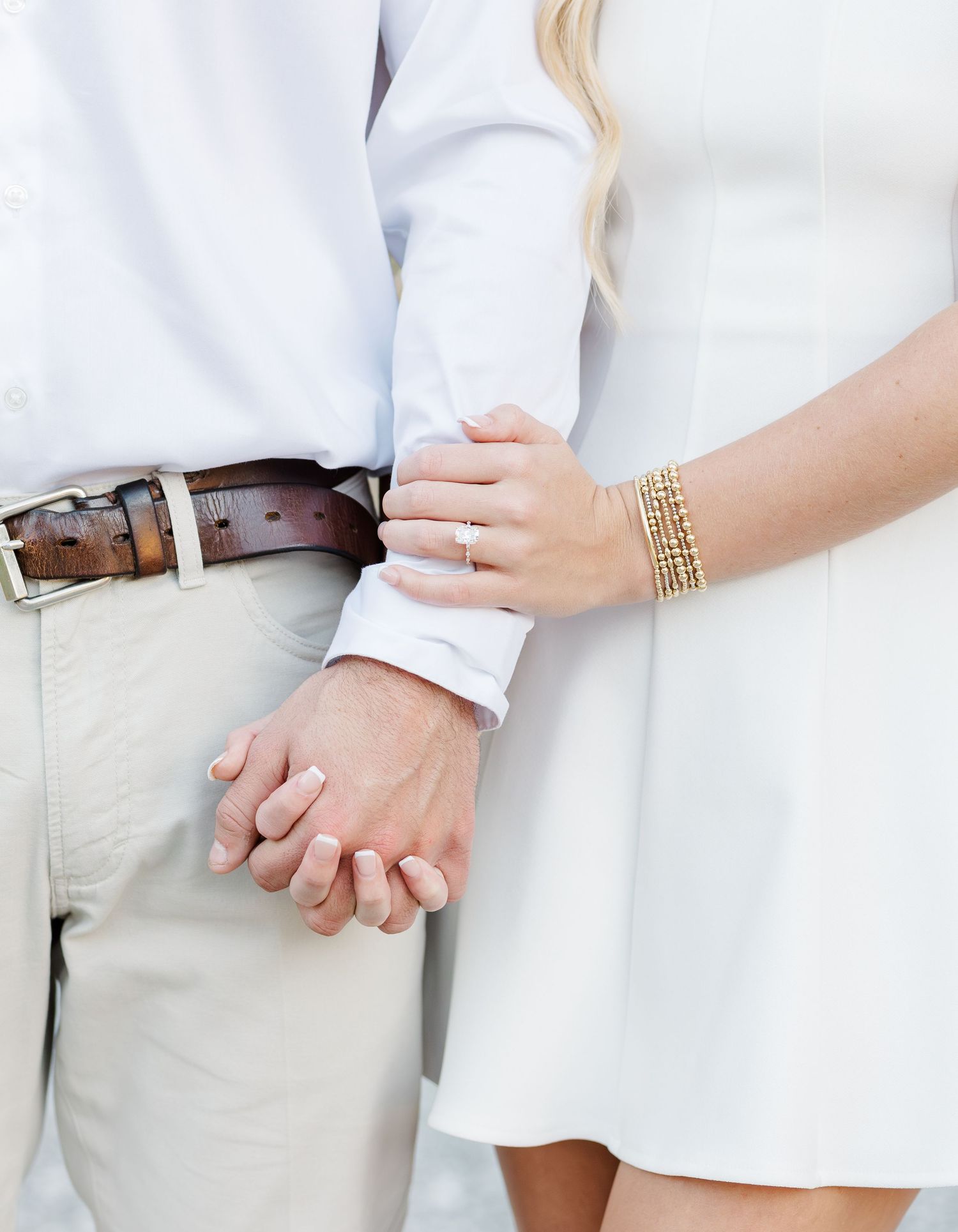 Close-up detail shot of hands wearing wedding rings against white and khaki clothing.