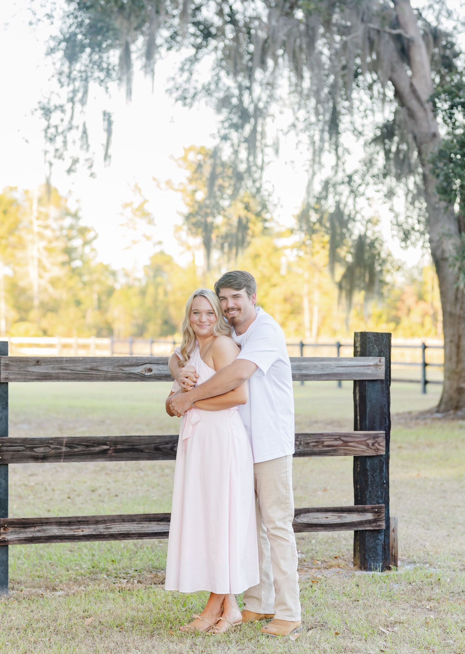 A romantic couple embraces in front of a rustic wooden fence on a sunny autumn day.