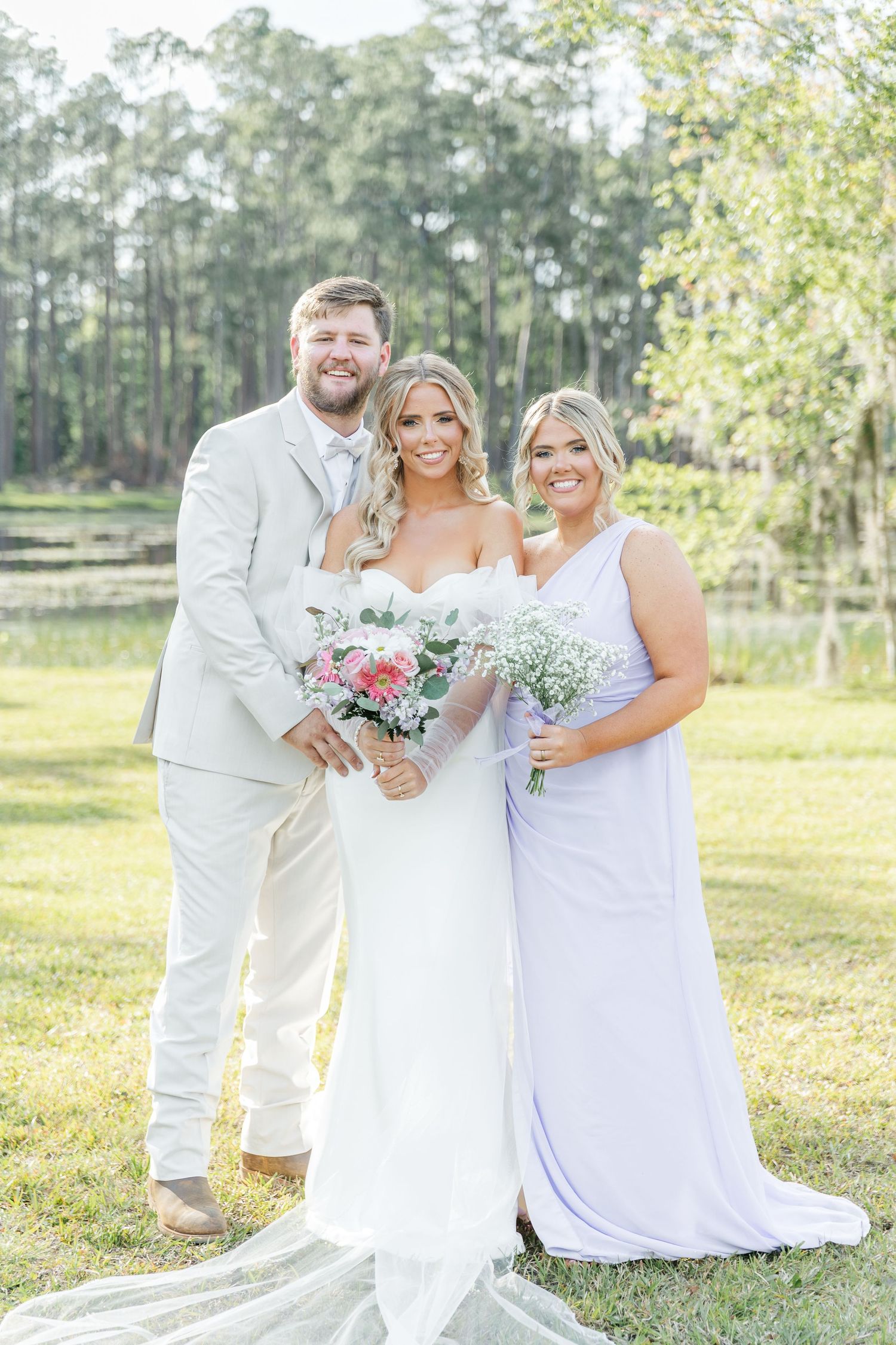 Elegant outdoor wedding photo with wedding party in white and lavender dresses holding floral bouquets.