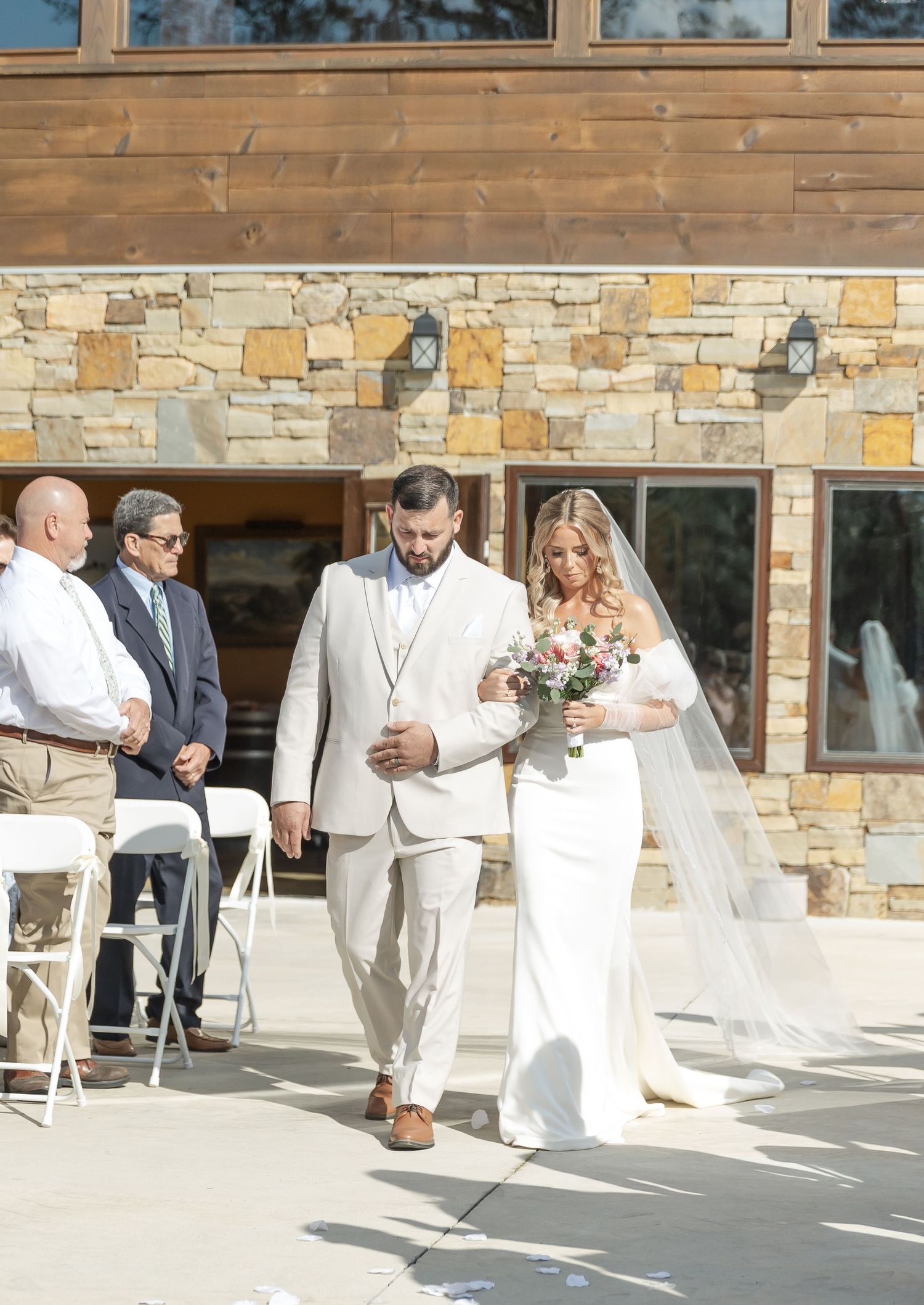 Couple exiting ceremony at rustic venue with stone walls and wooden details.