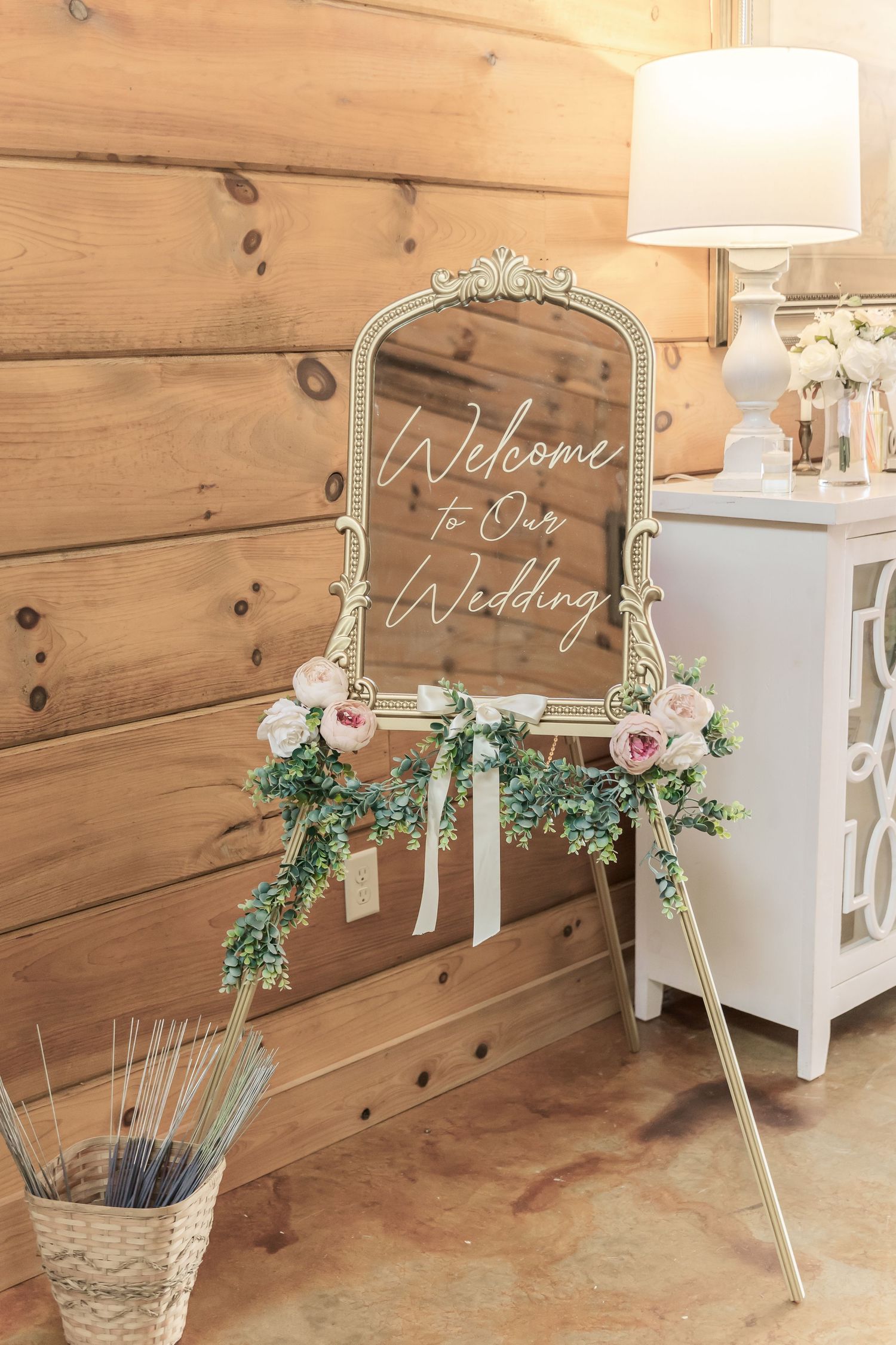 Decorative welcome mirror sign with floral accents against rustic wooden wall.