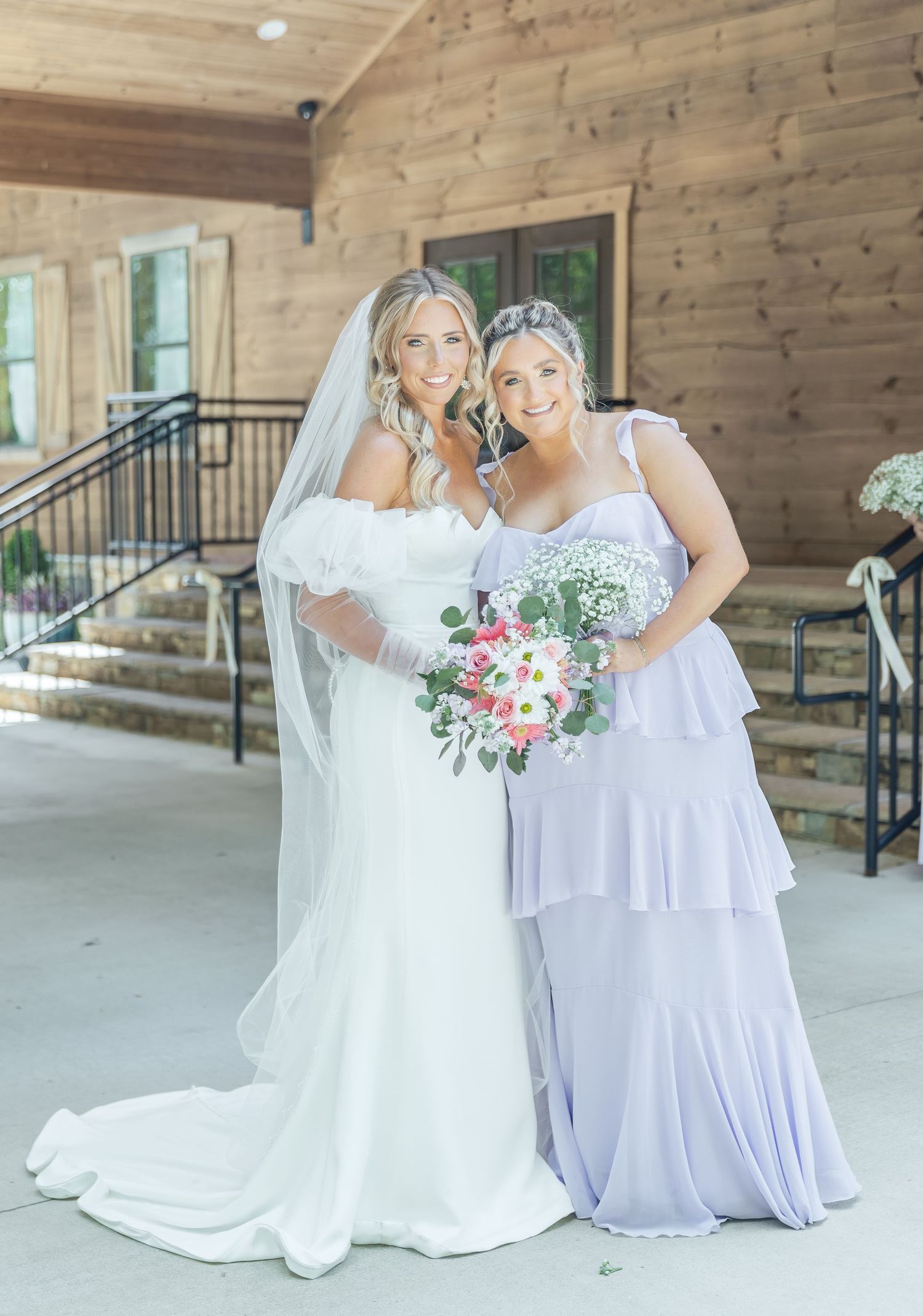 Wedding party members in white and lavender dresses share a moment on a covered porch.