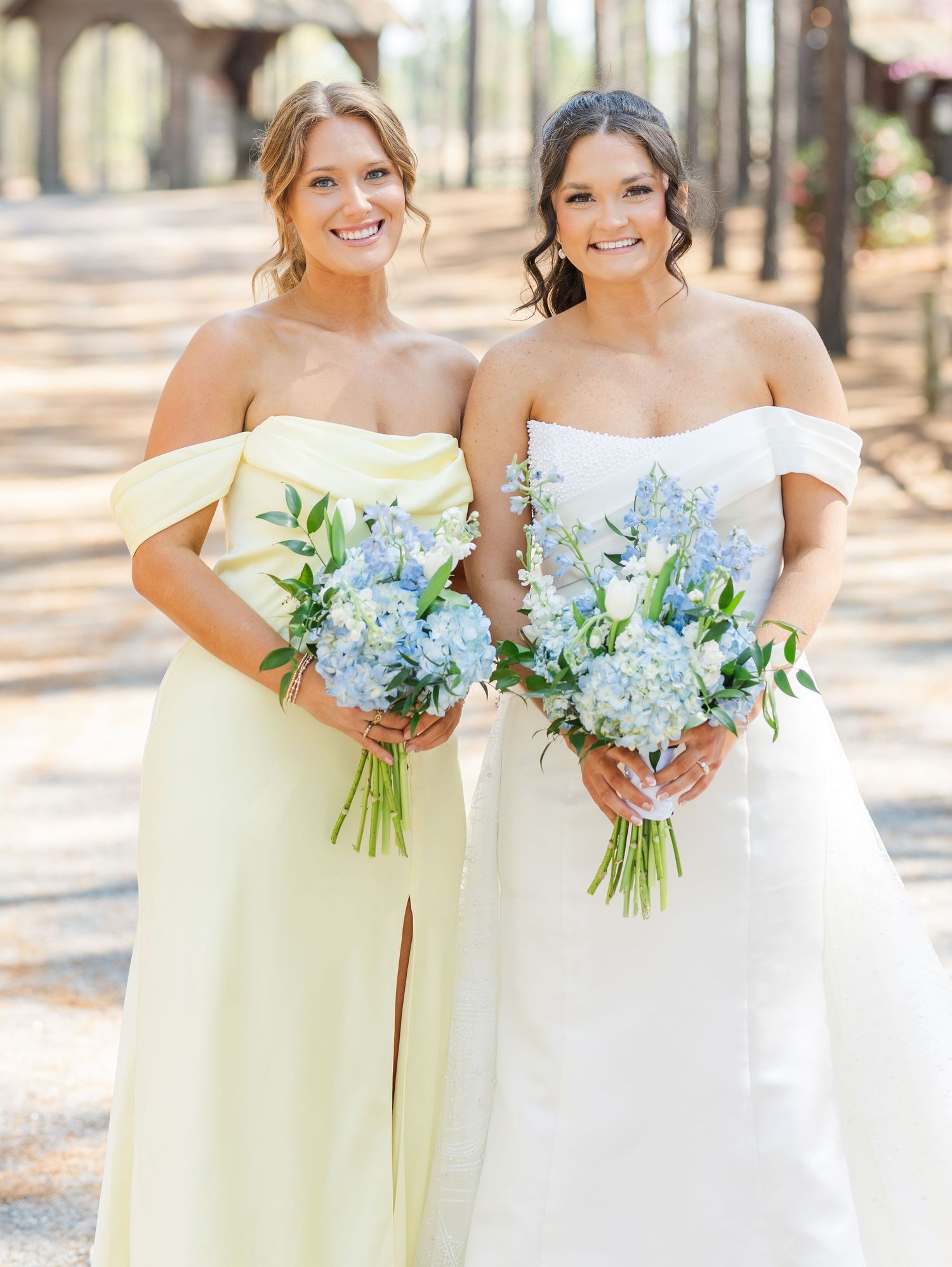Bride and bridesmaid in yellow off-shoulder gown holding matching blue hydrangea bouquets.