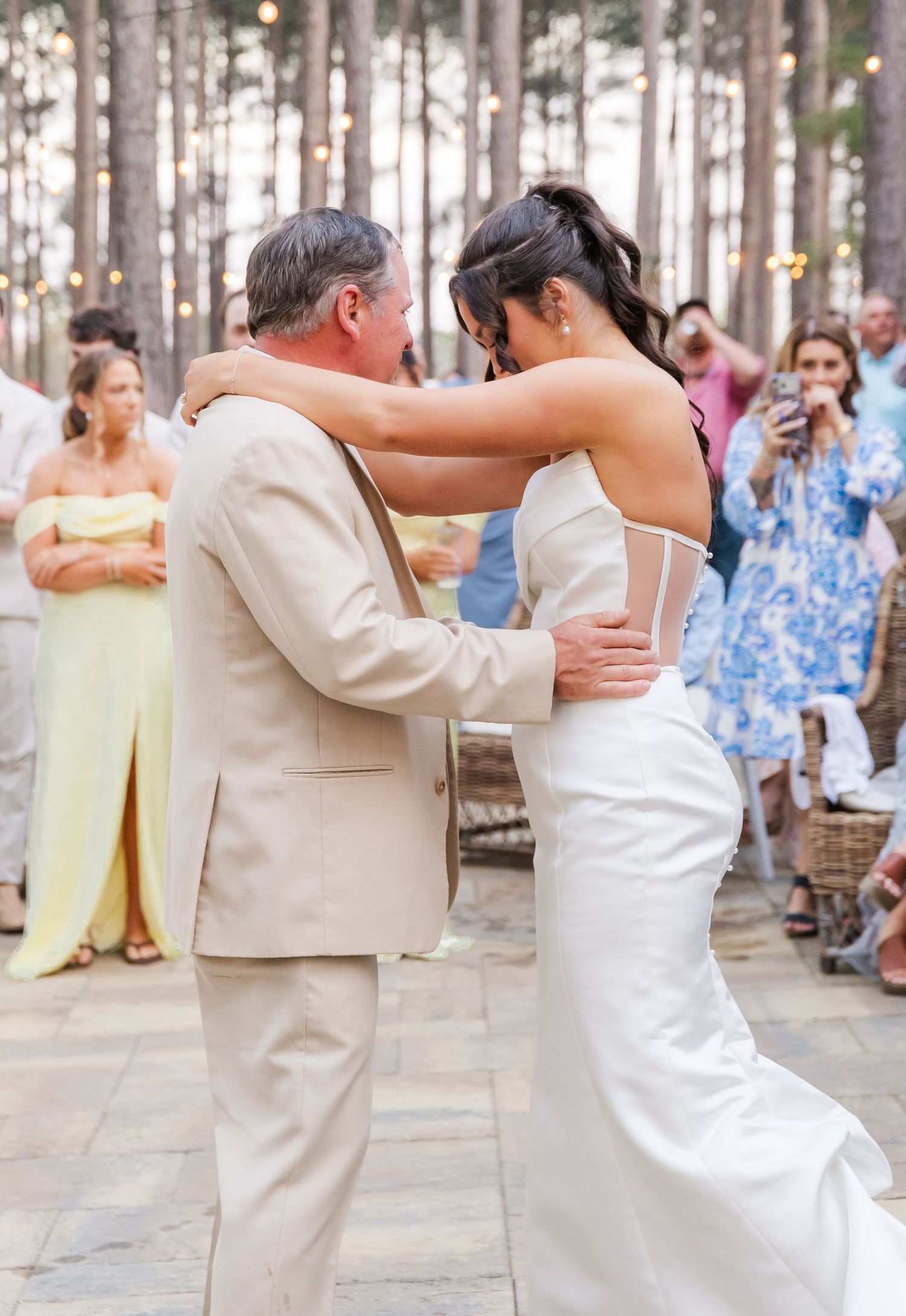 Bride sharing father-daughter dance outdoors at evening reception surrounded by string lights.