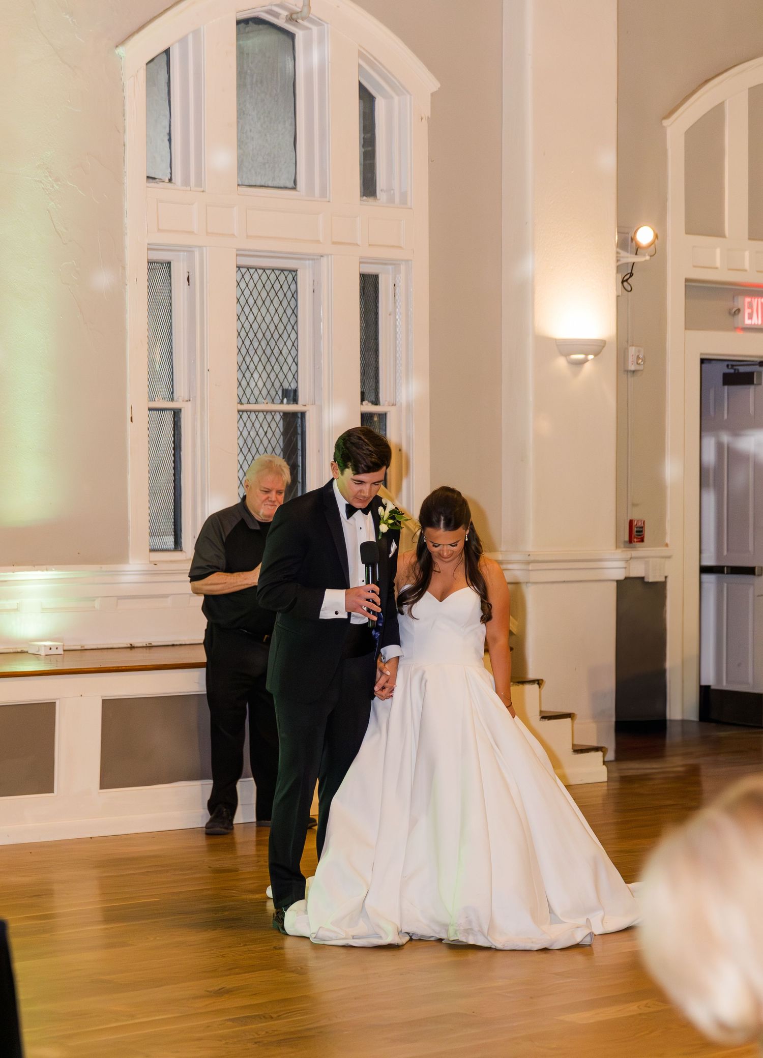 Bride and groom share an intimate first dance in elegant white wedding venue with arched windows.