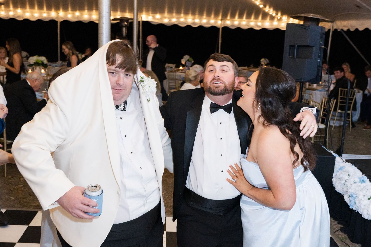 Groom and guests posing and laughing together on a black and white checkered dance floor at reception.