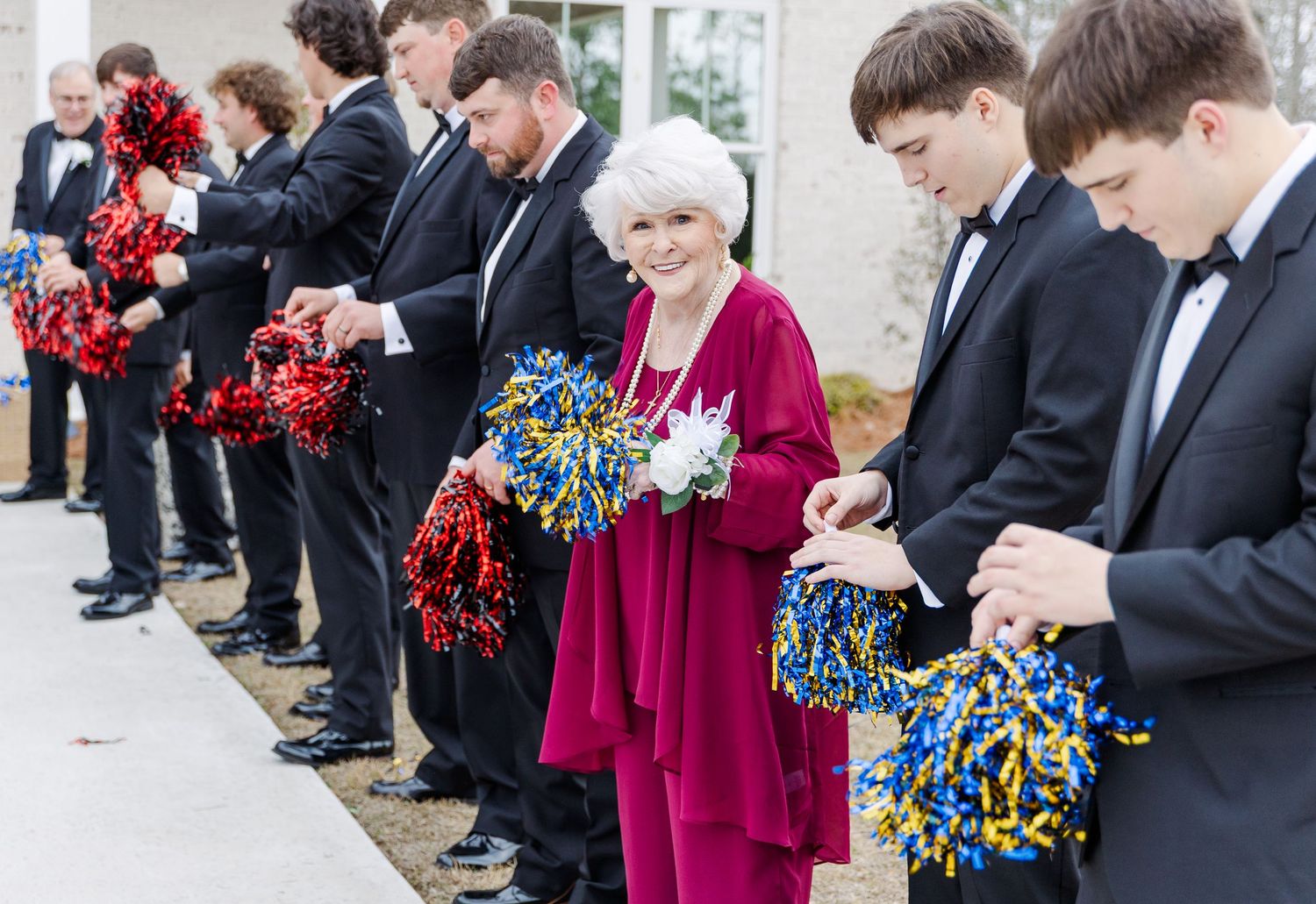 Wedding party line holding colorful pom-poms in red, blue and gold outside at wedding celebration.