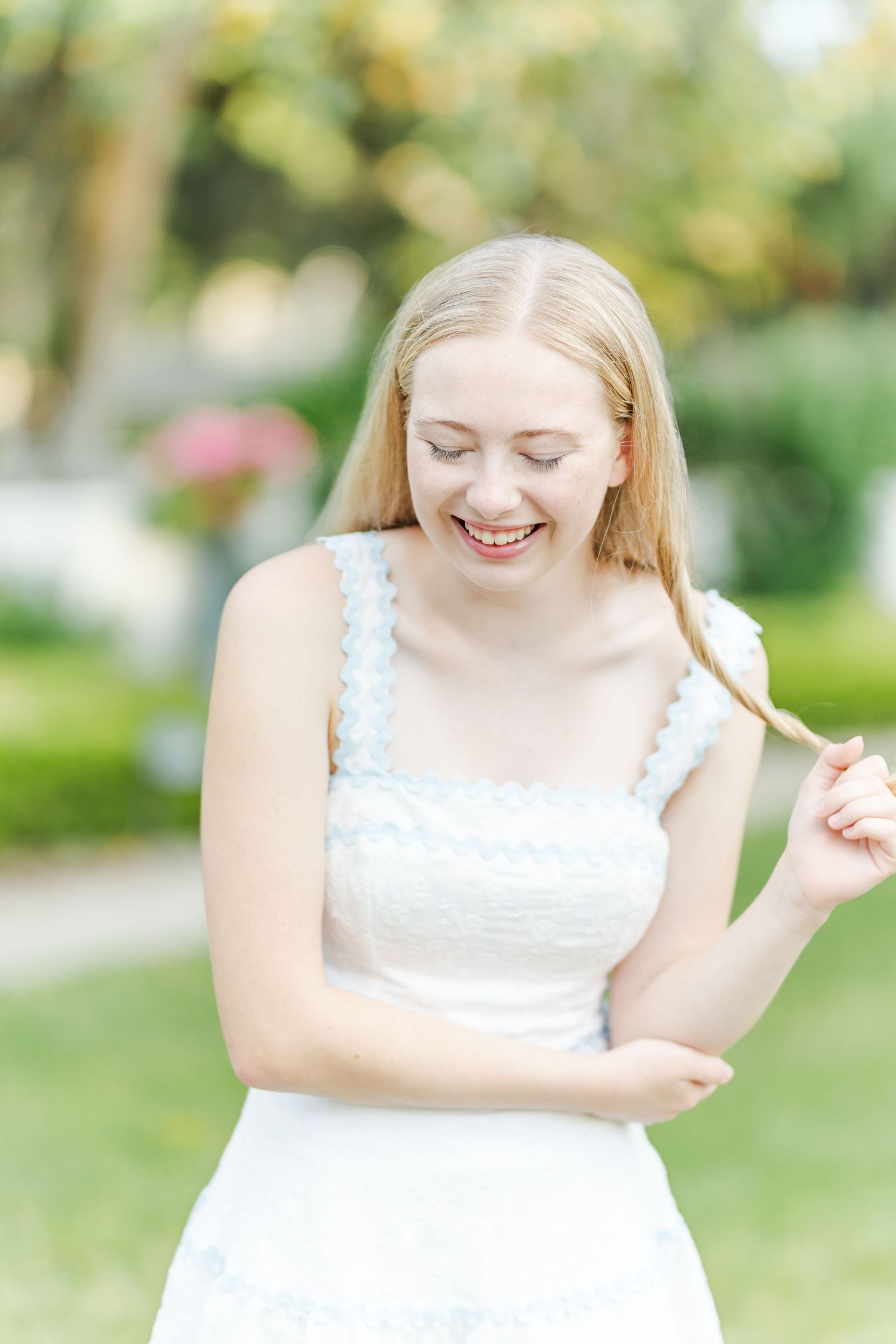 Person in delicate white summer dress poses joyfully in a sunlit garden setting.