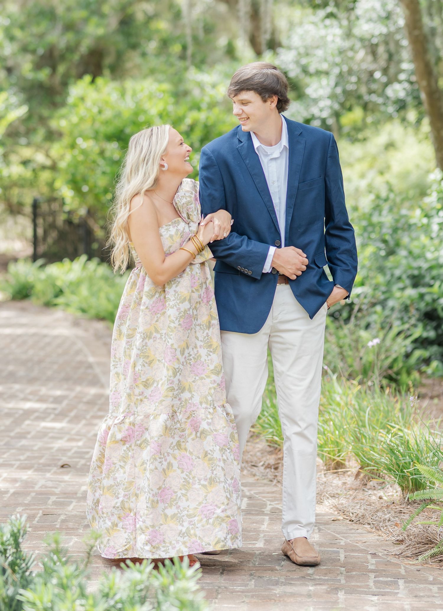 Couple in coordinated outfits sharing romantic moments on a brick pathway surrounded by gardens.