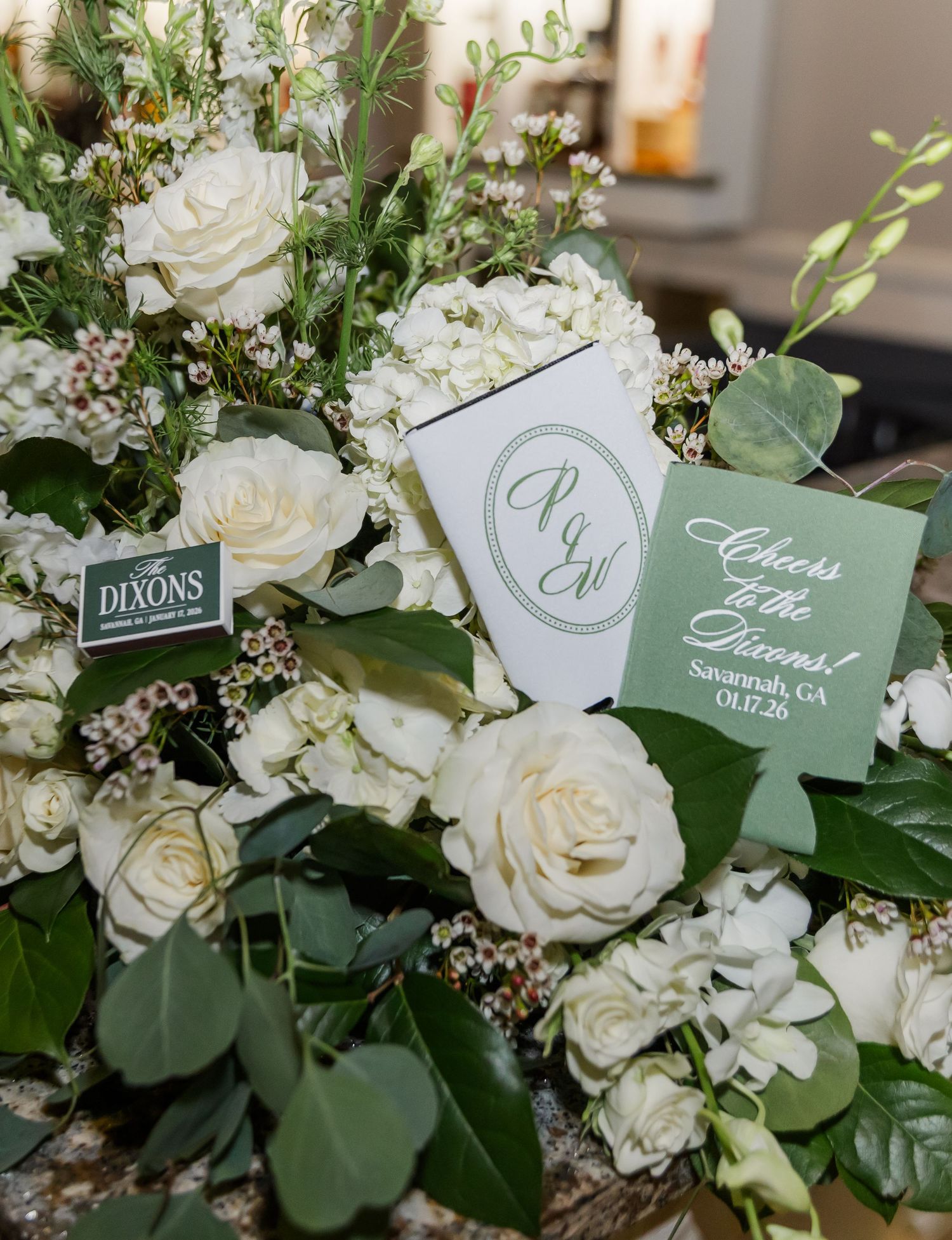 White roses and greenery arrangement with sage green name cards for wedding table settings.