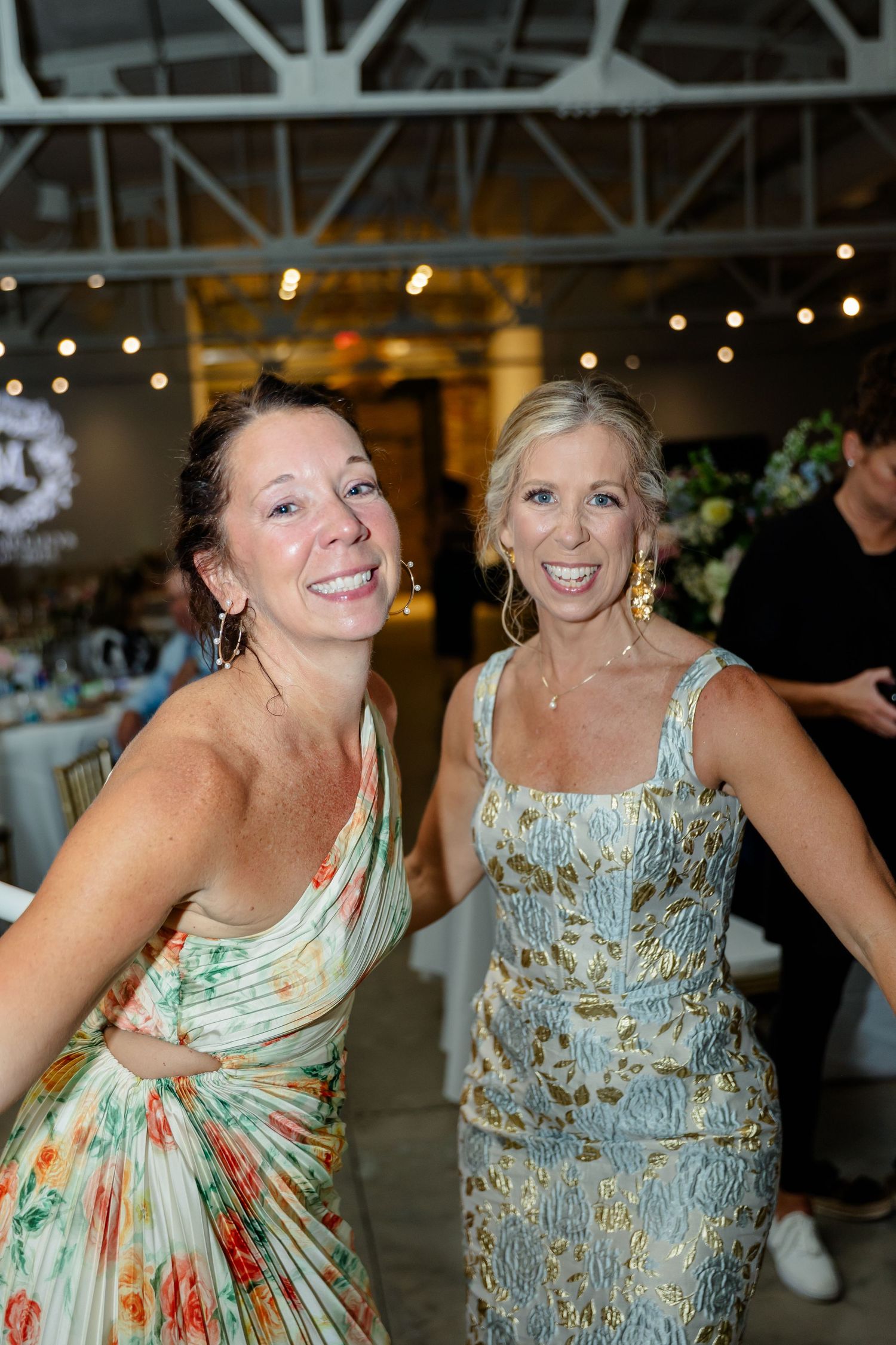 Wedding guests dancing and laughing together at a reception with string lights and industrial decor.