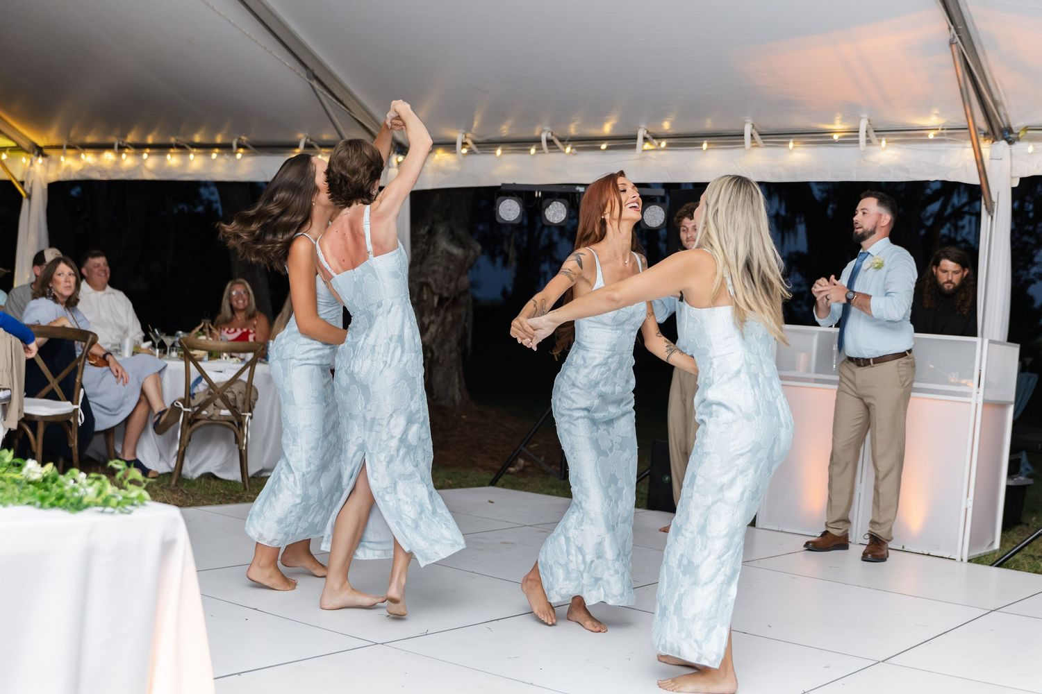 Guests dancing in formal attire under string lights at an outdoor wedding reception.