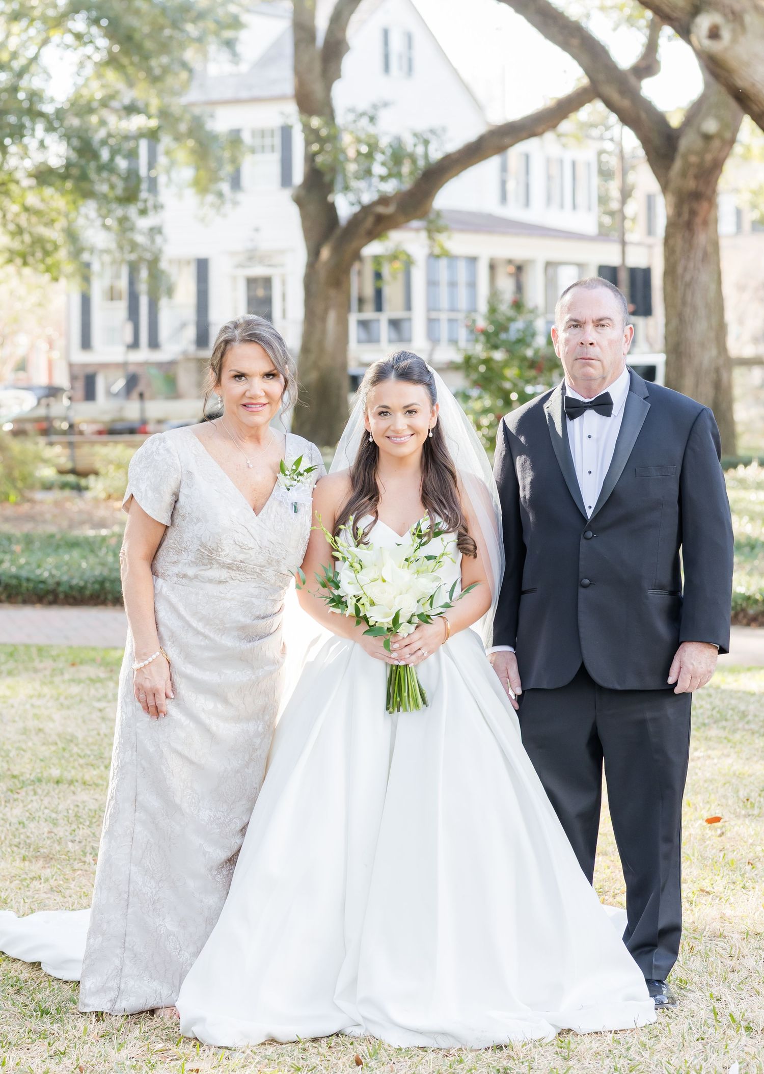Wedding party members pose for formal portraits under oak trees on a sunny day.