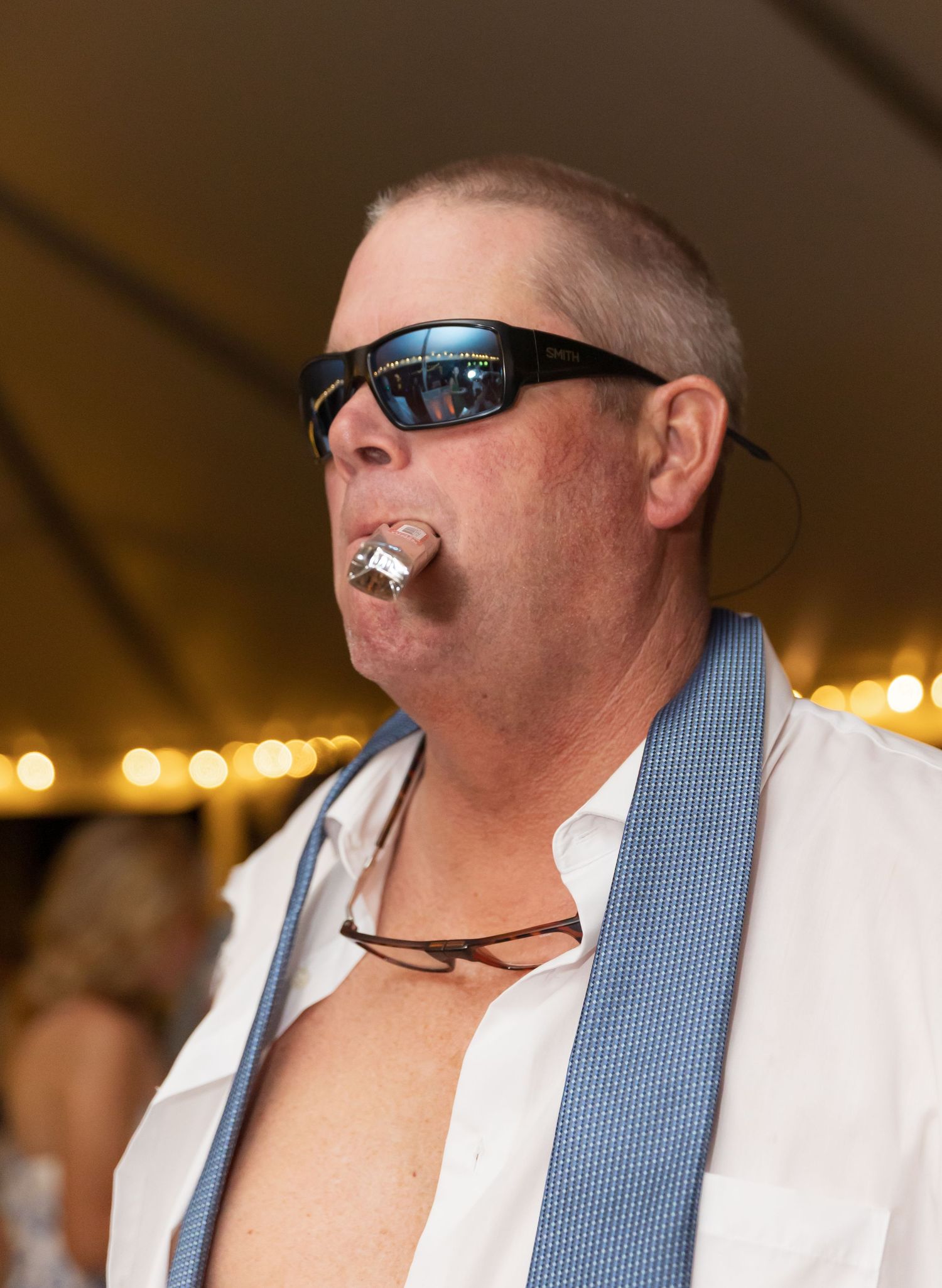 Wedding guest in a white shirt and blue tie enjoying drinks at an outdoor reception.