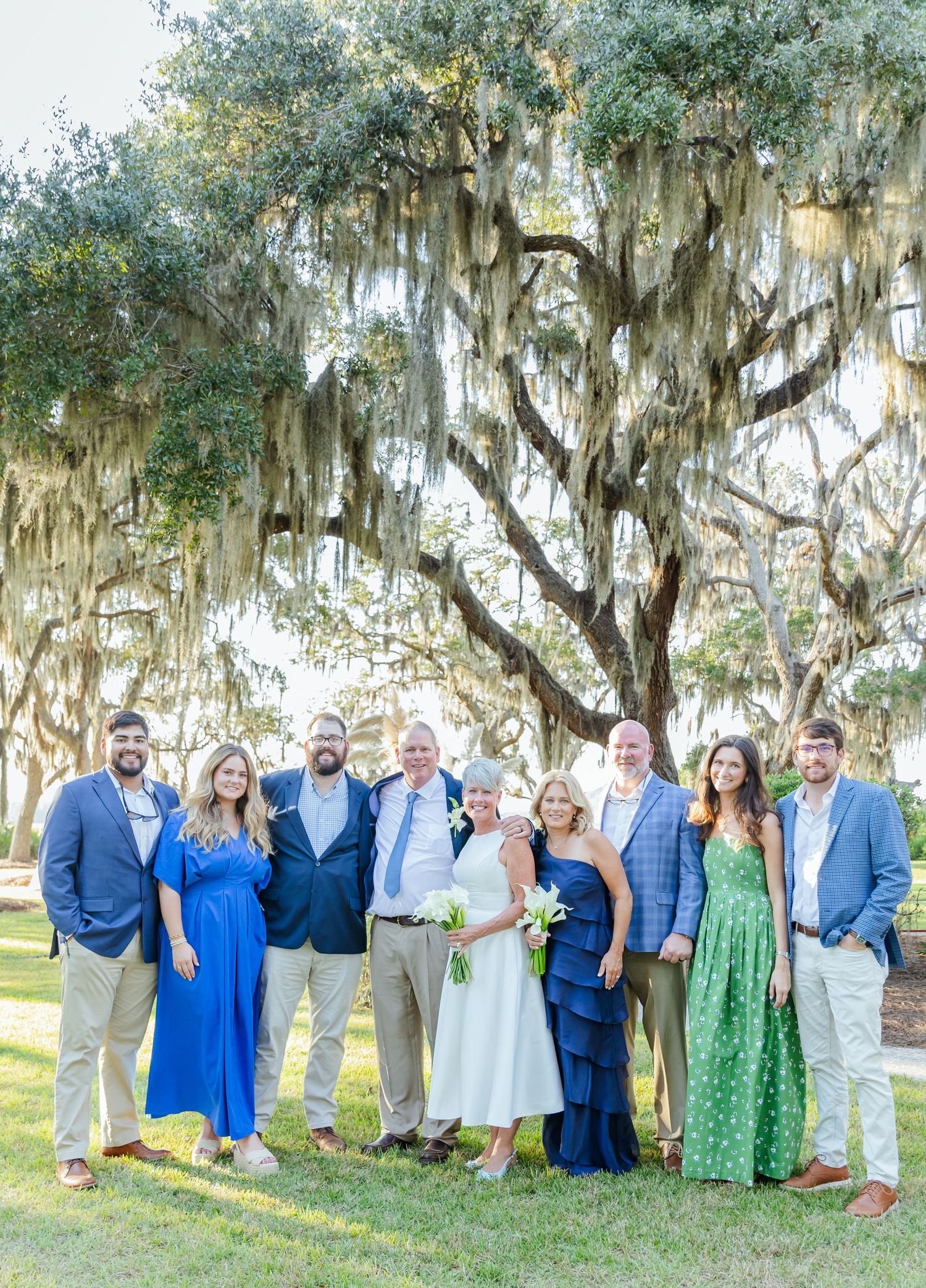 Large family group gathers for outdoor portrait under moss-covered oak trees in coordinated blue and white outfits.