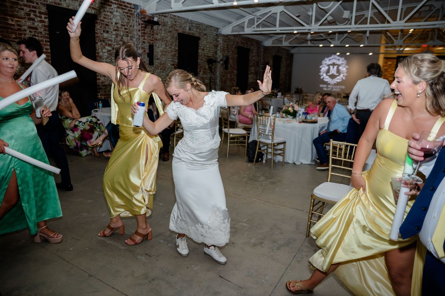 Wedding reception guests dancing and celebrating on a dance floor in an indoor venue.