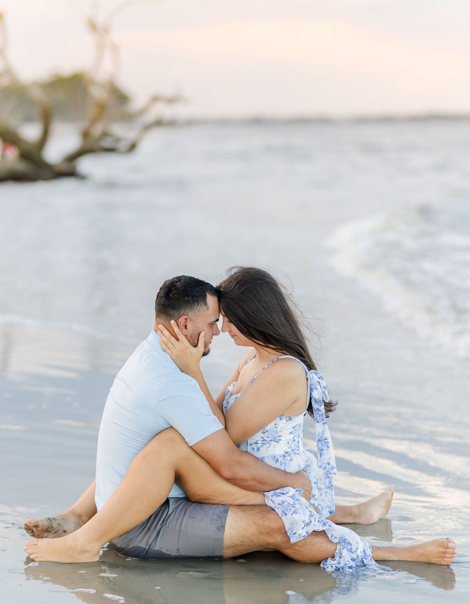 A couple in soft pastel tones embraces intimately on a sandy beach during sunrise creating a romantic silhouette.