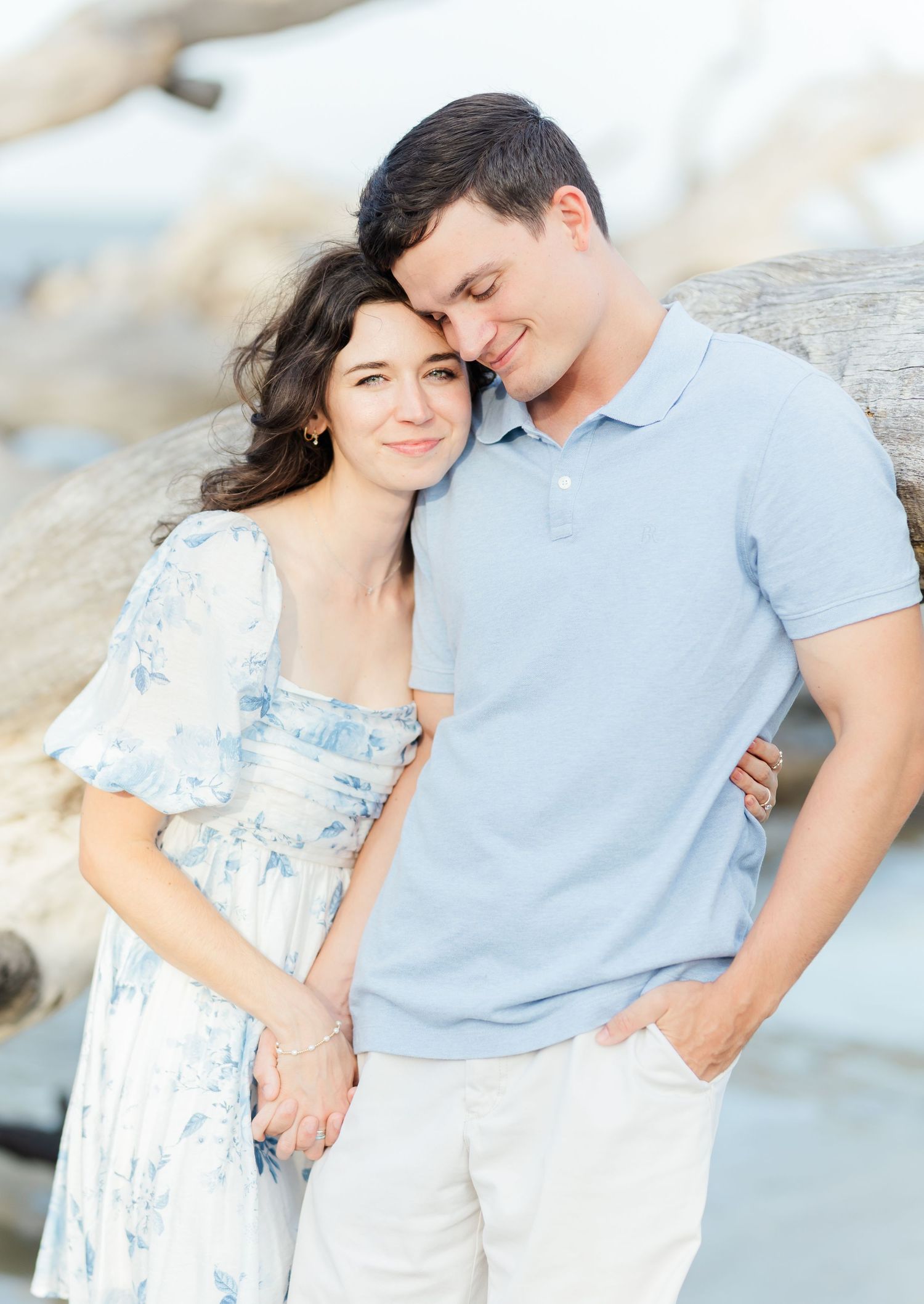 Romantic couple in coordinated blue and white outfits pose together against rocky coastal backdrop during sunset photoshoot.