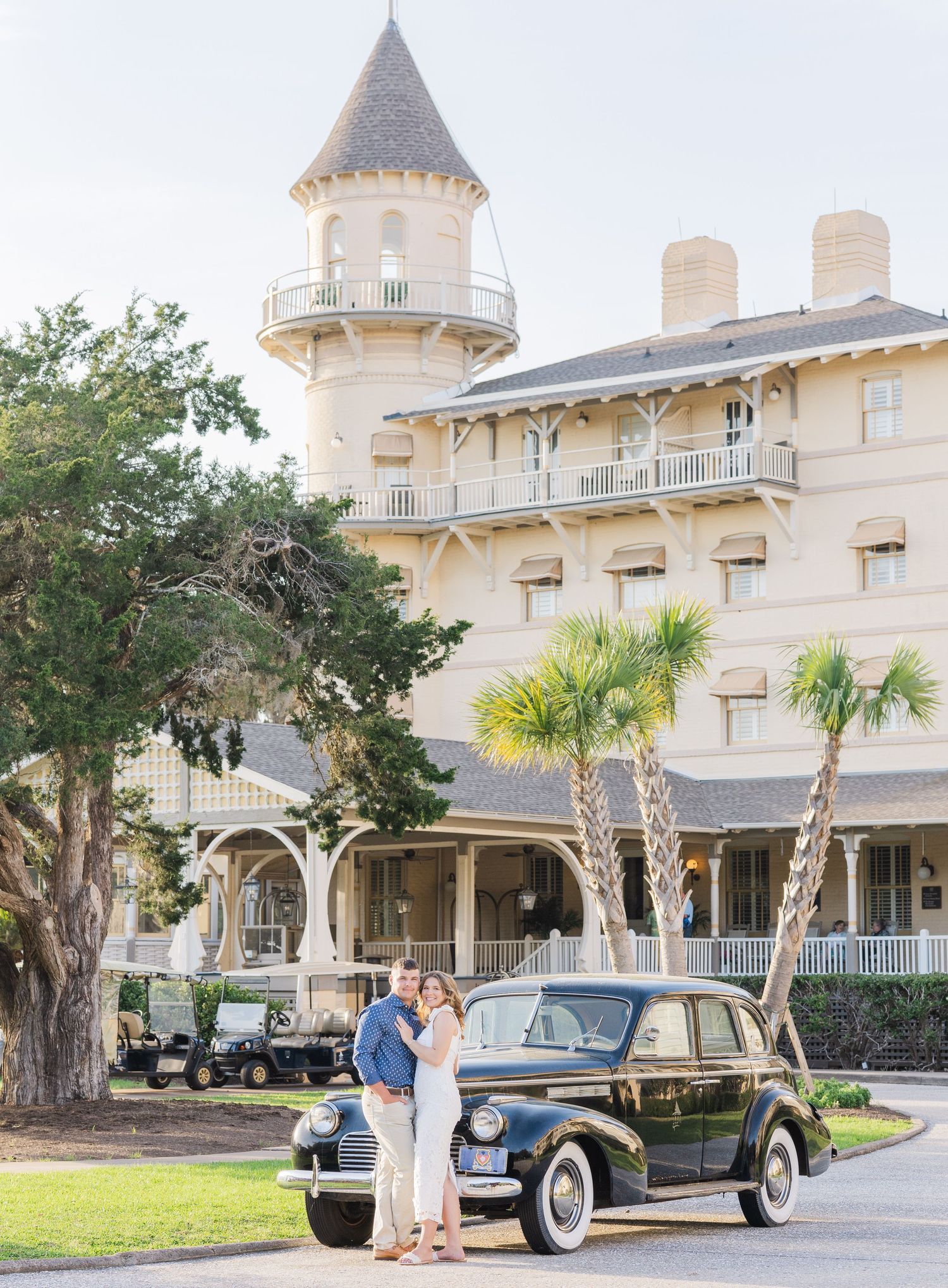 Elegant vintage car parked in front of a grand Victorian-style mansion with palm trees and manicured grounds.