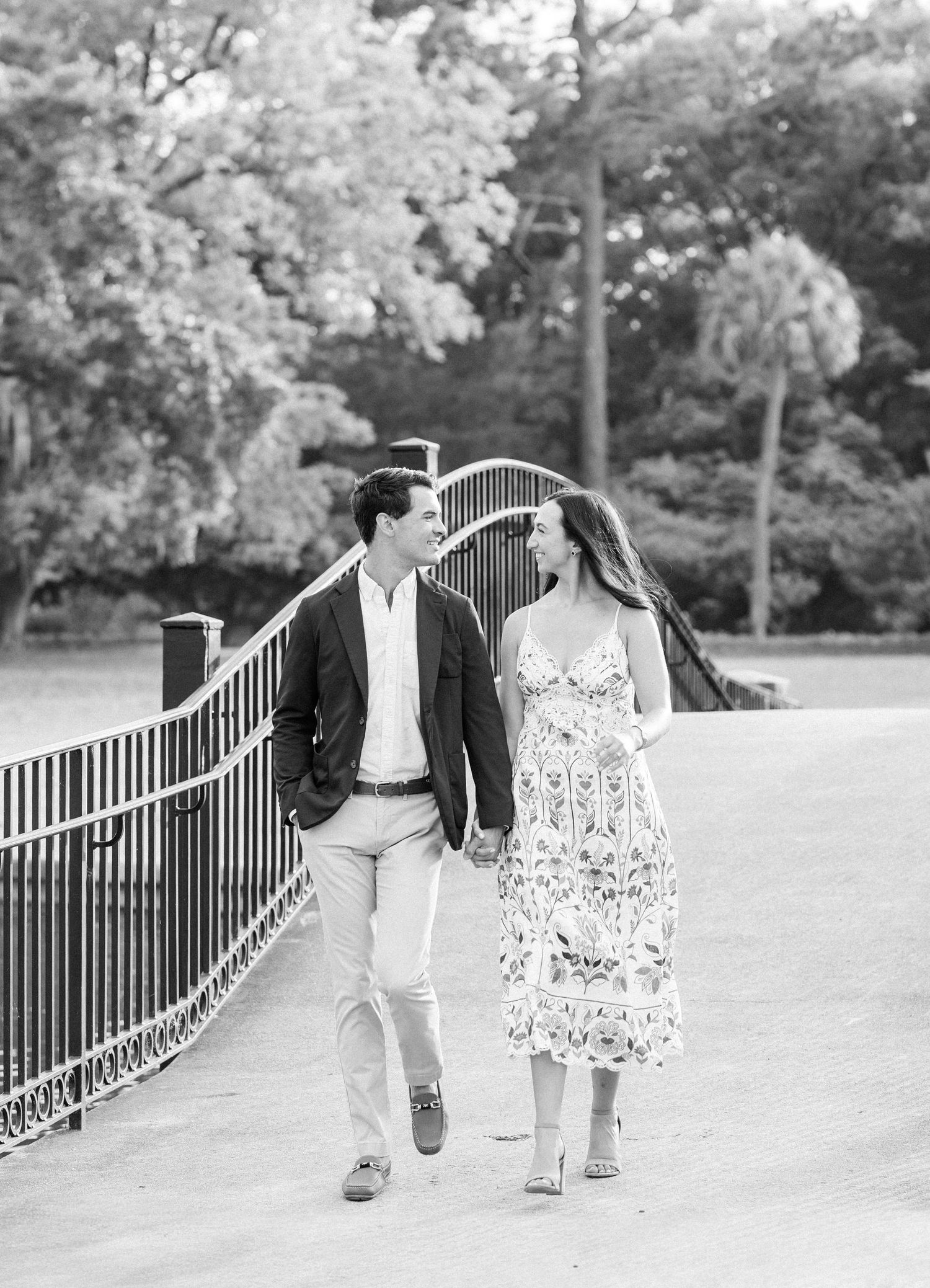 Black and white photo of couple holding hands and walking along a curved iron fence path.