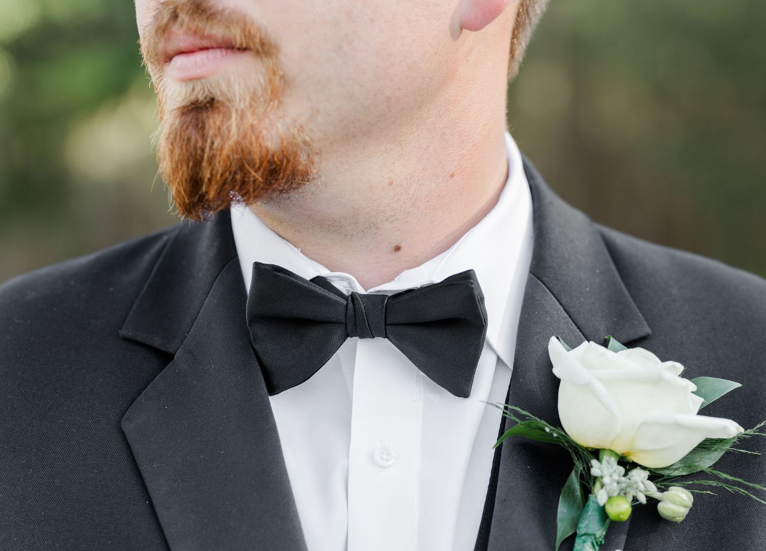 Groom in black tuxedo with bow tie and white rose boutonniere with baby's breath detail.