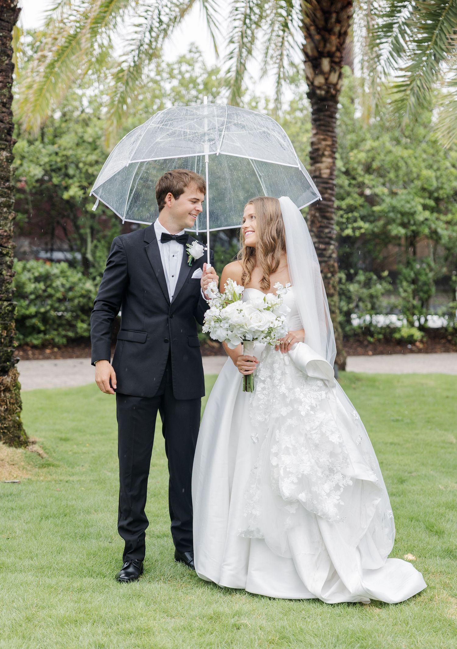 Bride and groom sharing a romantic moment under a clear umbrella on rainy wedding day.