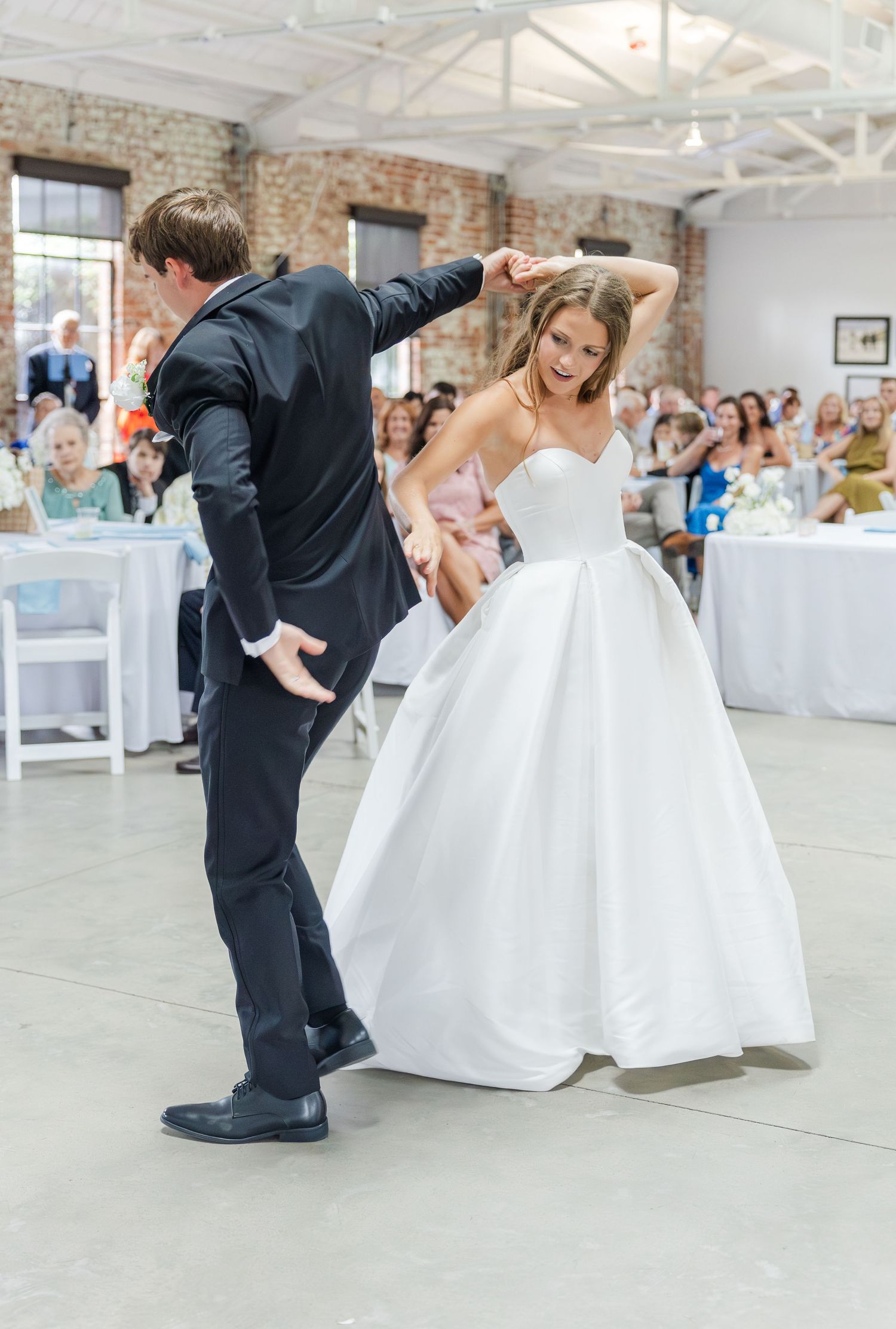 Bride in white ball gown twirls during first dance with groom in black suit at elegant wedding reception.