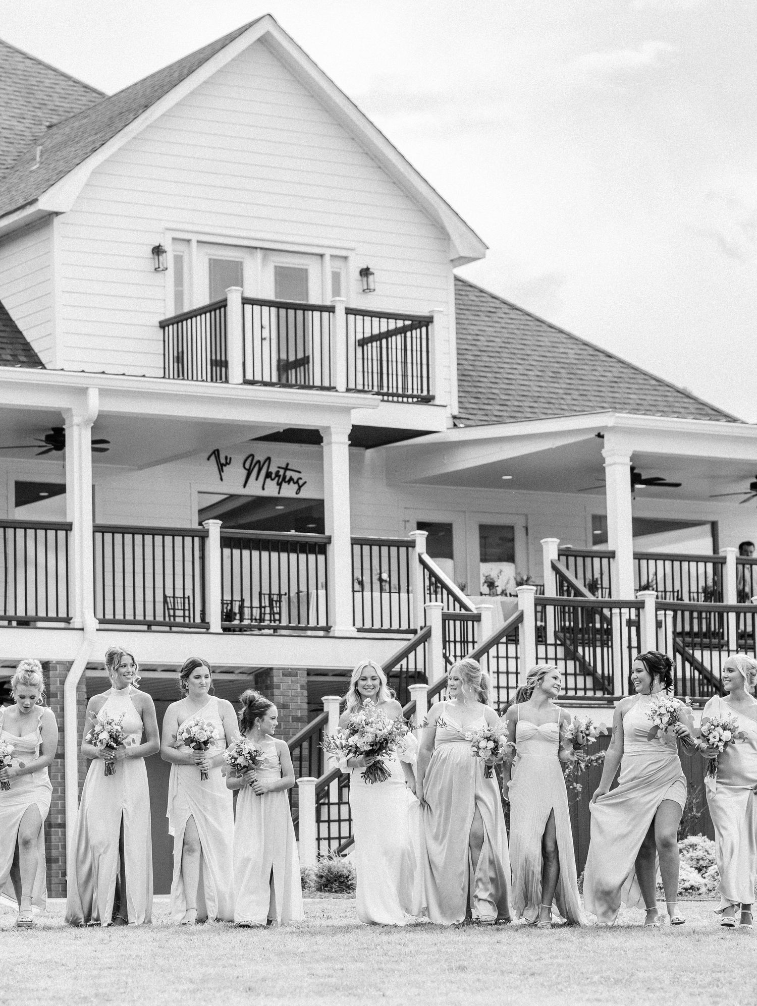 Black and white photo of bridal party in matching gowns posing in front of a white two-story wedding venue.