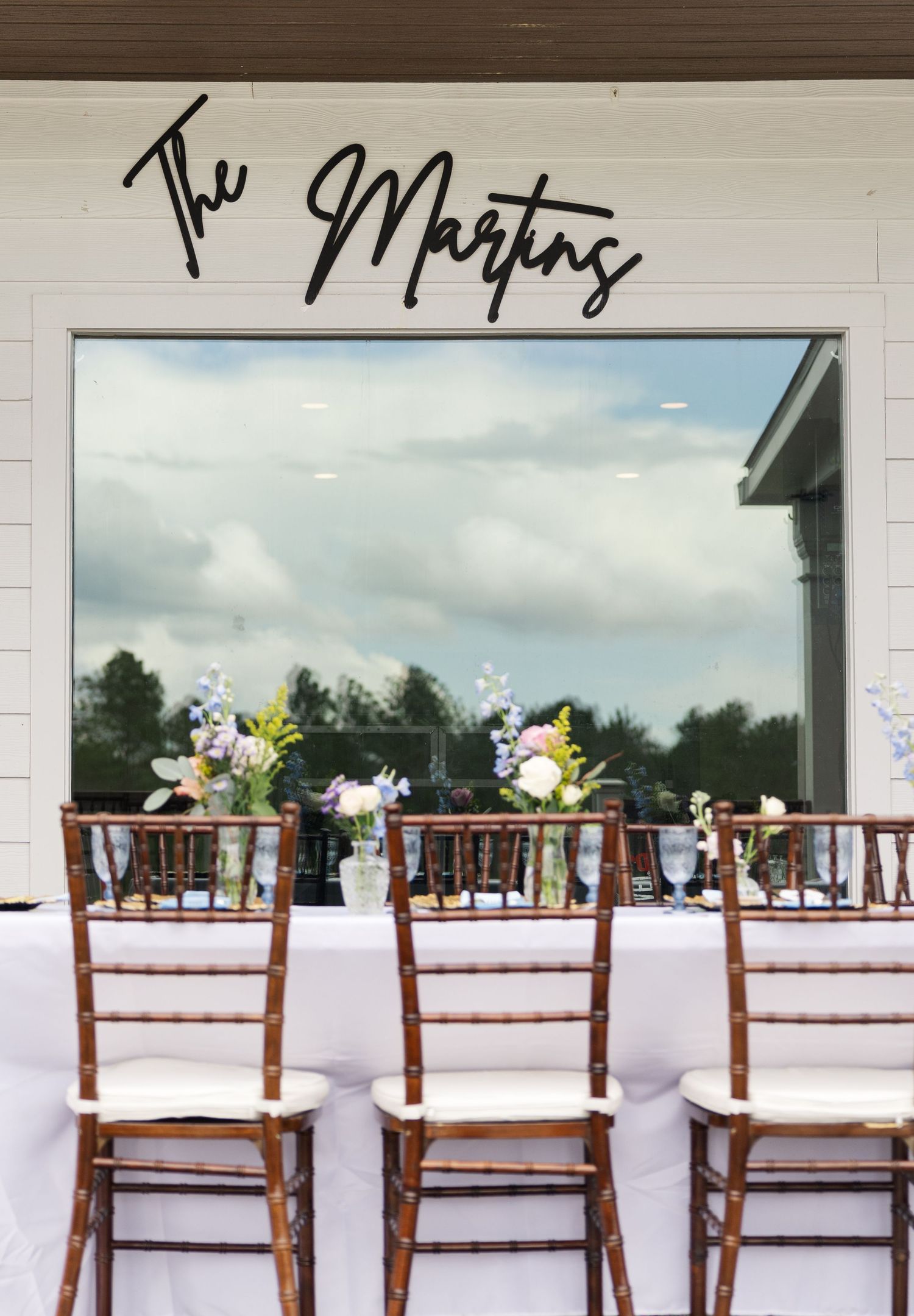 Wedding sweetheart table with chiavari chairs beneath a custom black script The Martins sign.