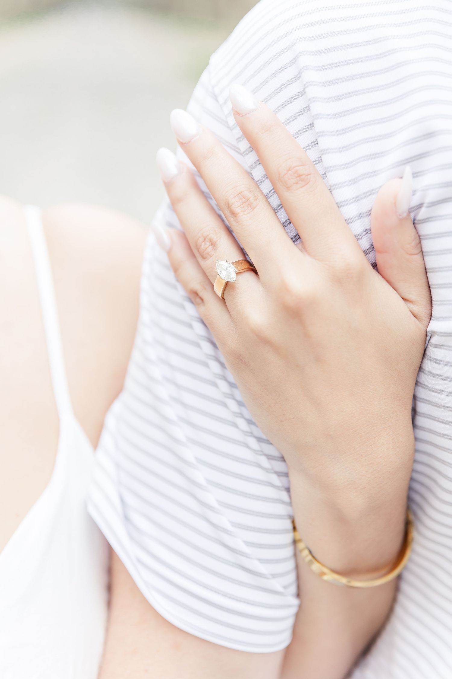 Close-up of an elegant hand wearing a gold ring and bracelet against a white striped fabric background.