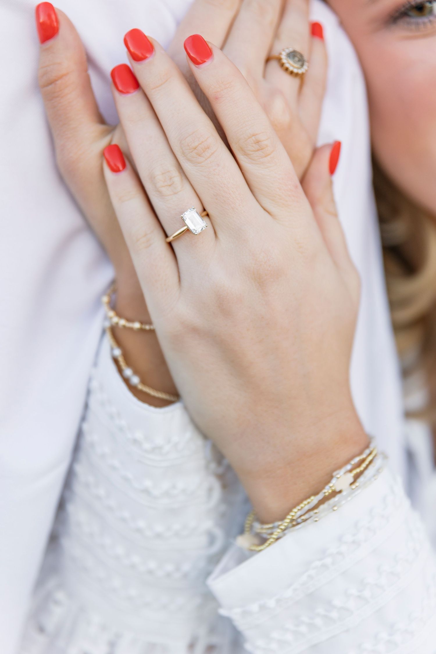 A close up of hands with red nail polish showing off an engagement ring and bracelets.