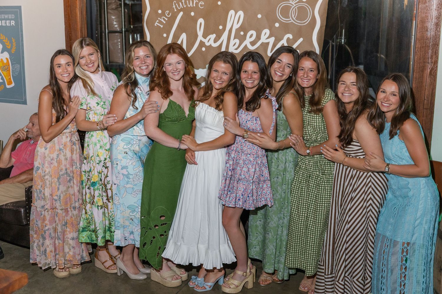 Group of ten women in colorful dresses posing together at a bachelorette party celebration.