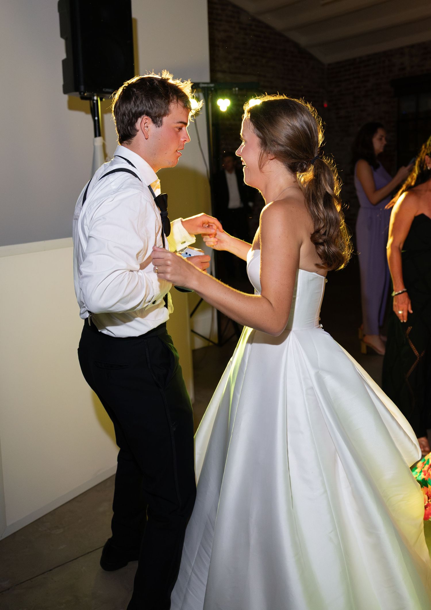 Bride in white ballgown and groom in white shirt dancing joyfully at wedding reception.