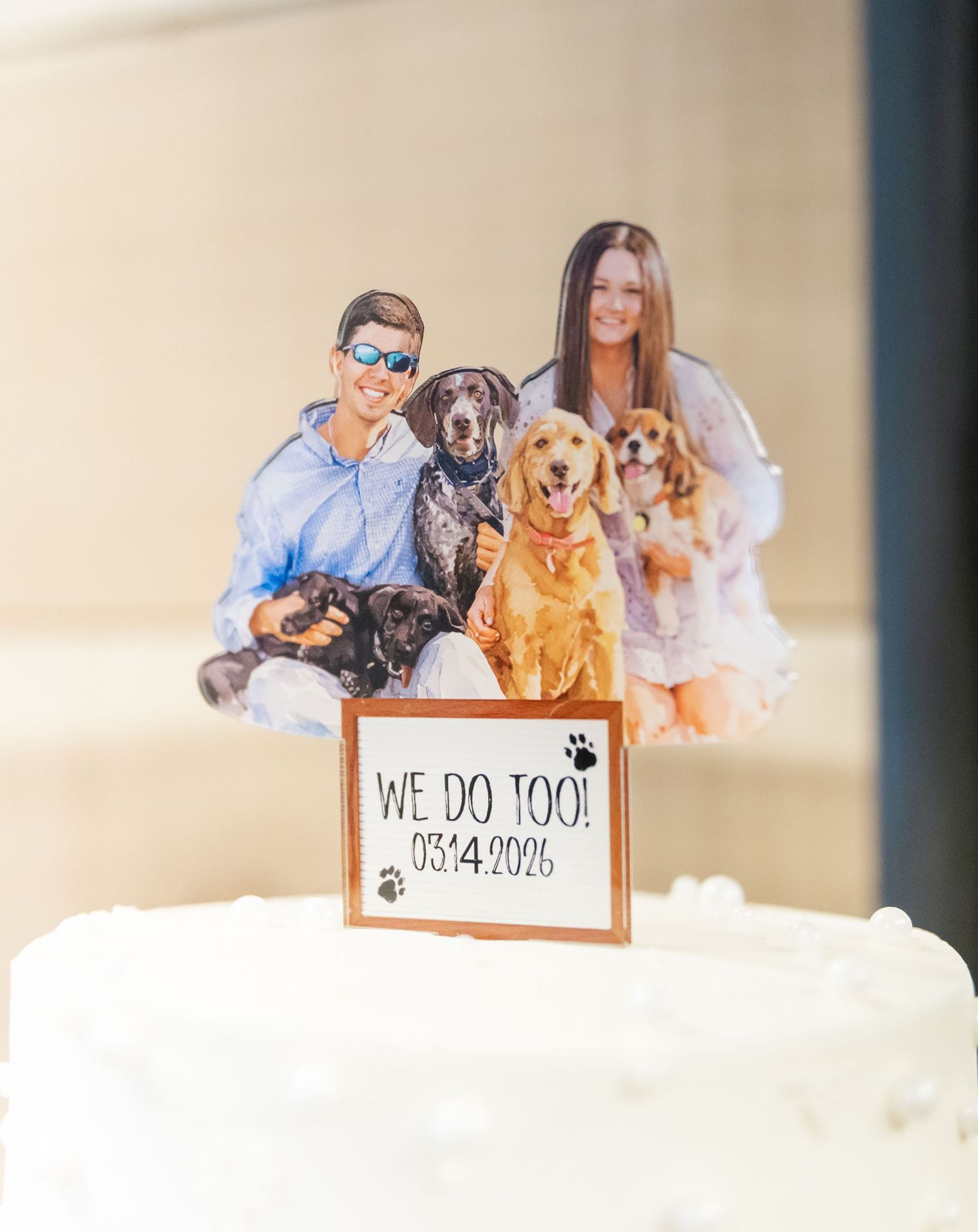 Custom wedding cake topper featuring couple with their dogs and a sign reading We Do Too 03.4.2026.