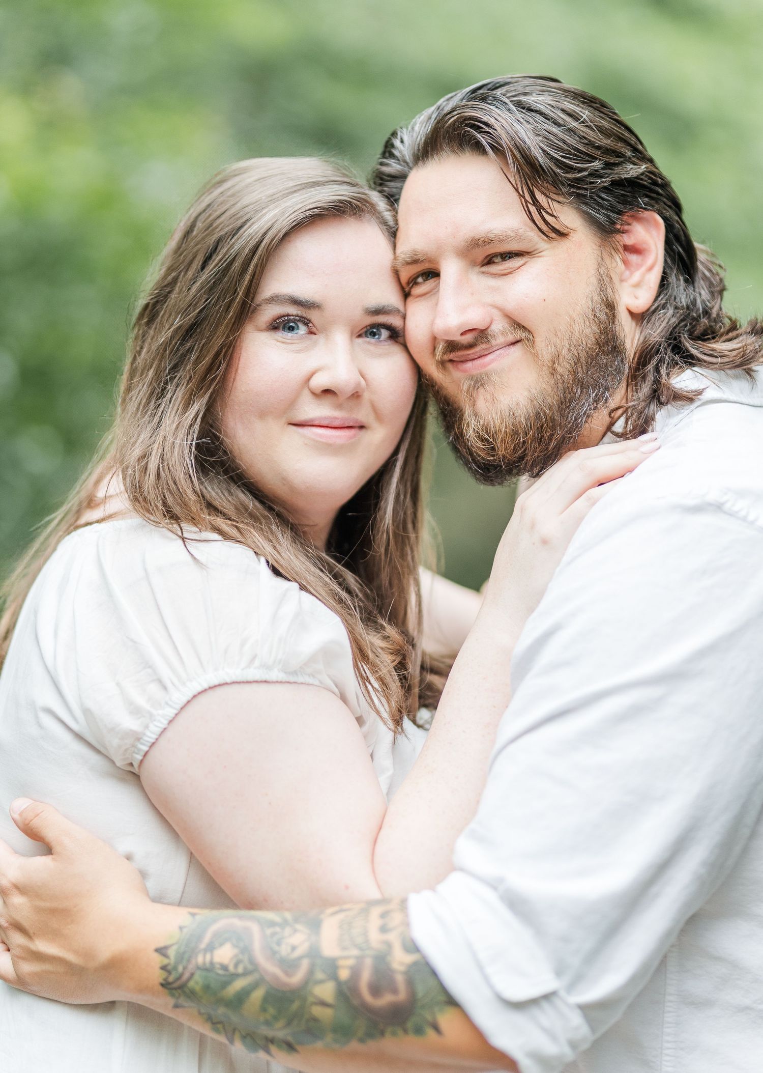 A close-up portrait of a couple embracing with natural greenery in the background.