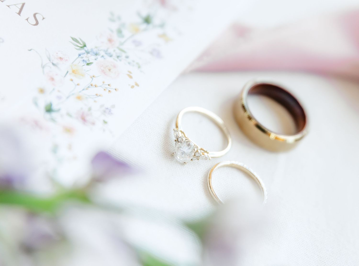Three elegant wedding rings arranged on a white surface with delicate floral details in soft focus.
