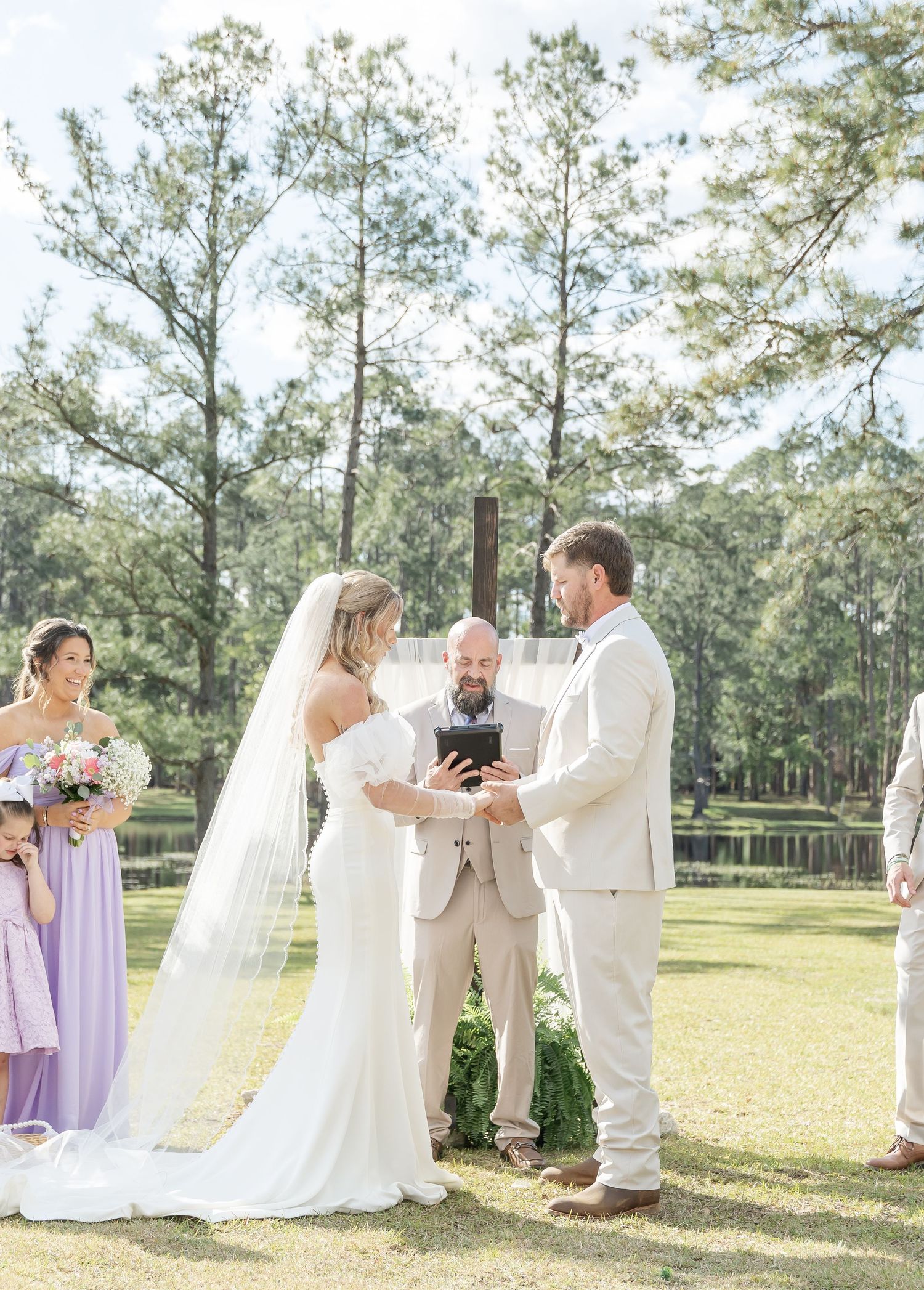 Intimate outdoor wedding ceremony with couple and officiant framed by tall pine trees.