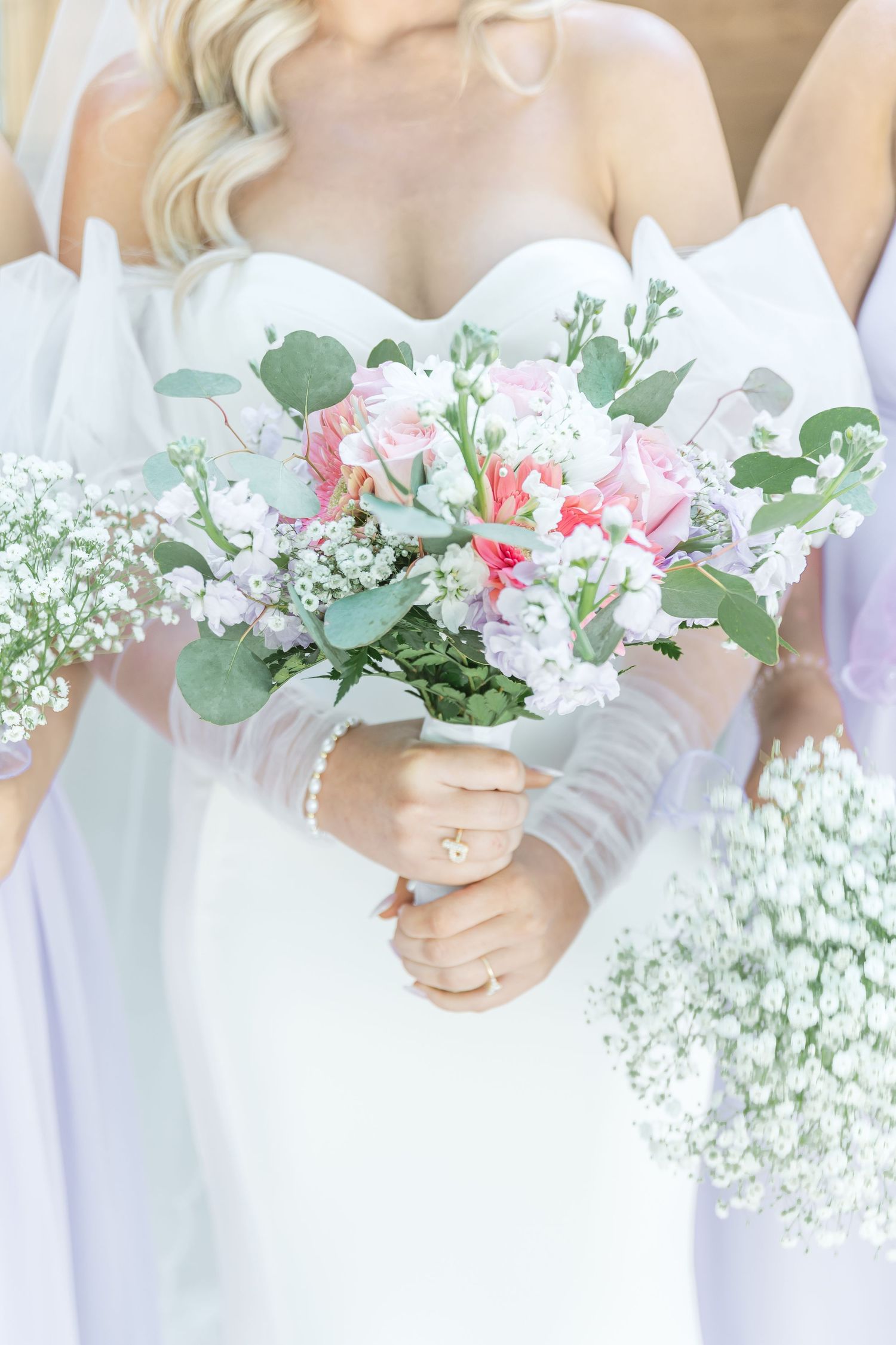 Elegant bridal bouquet featuring pink and white flowers with eucalyptus against white wedding dress.